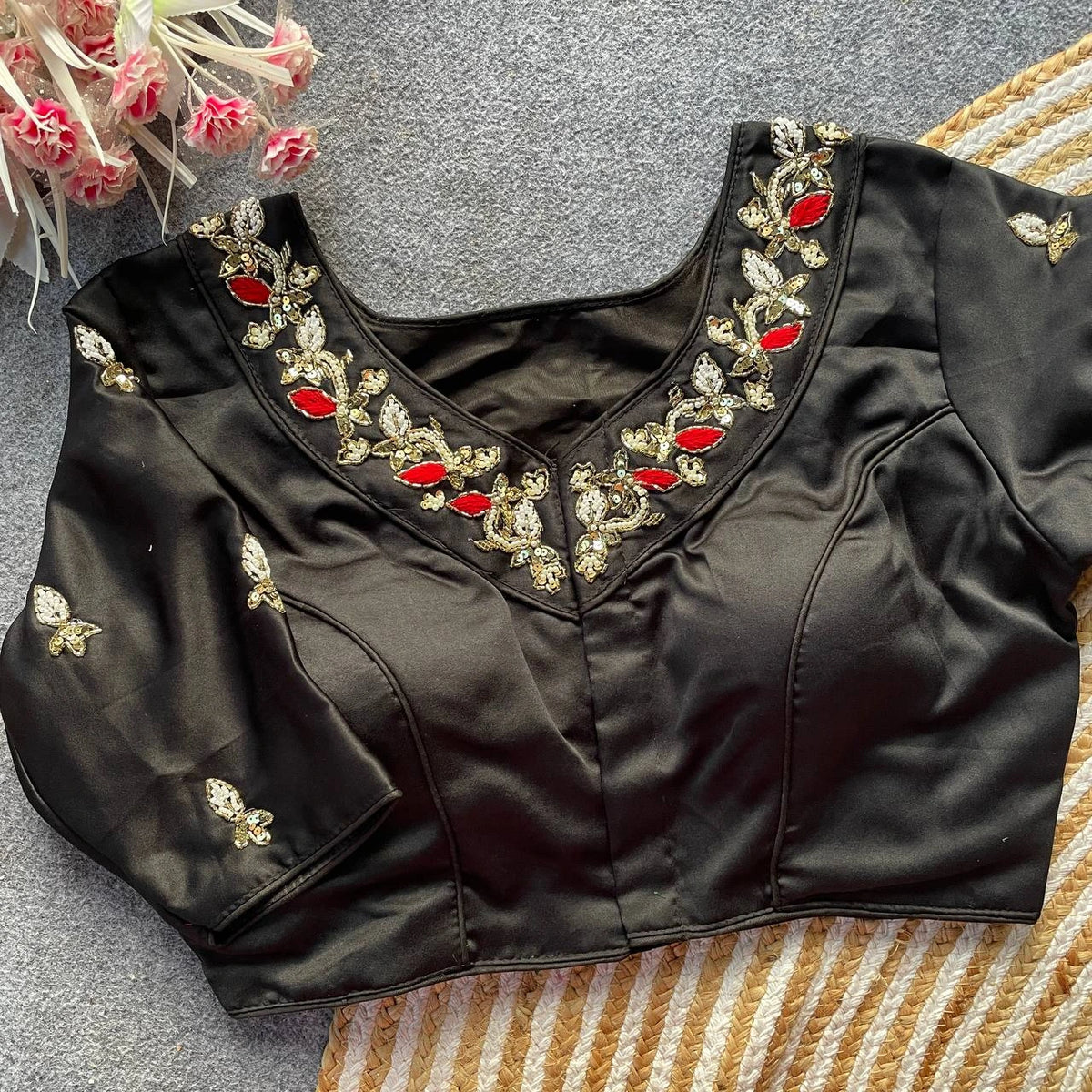 Black blouse with intricate gold and red embroidery on a textured surface.