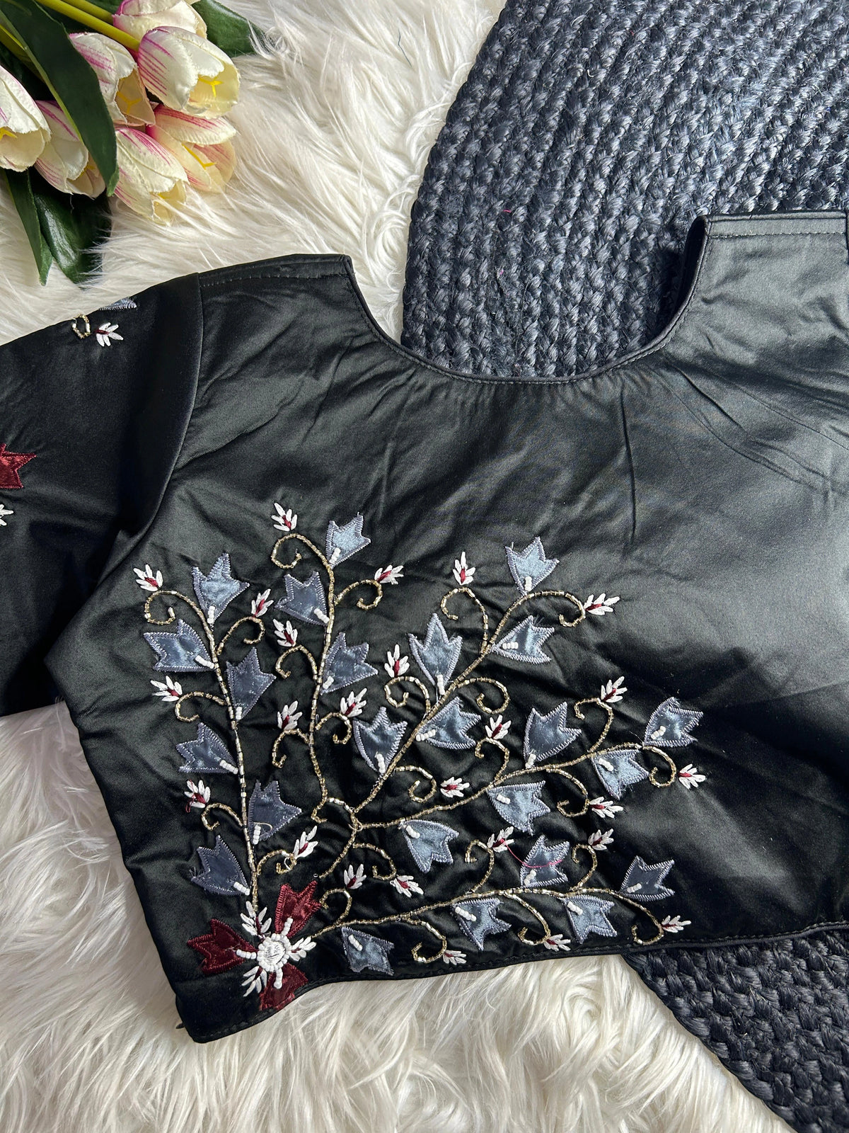 Black jacket with floral embroidery on a textured surface with flowers in the background