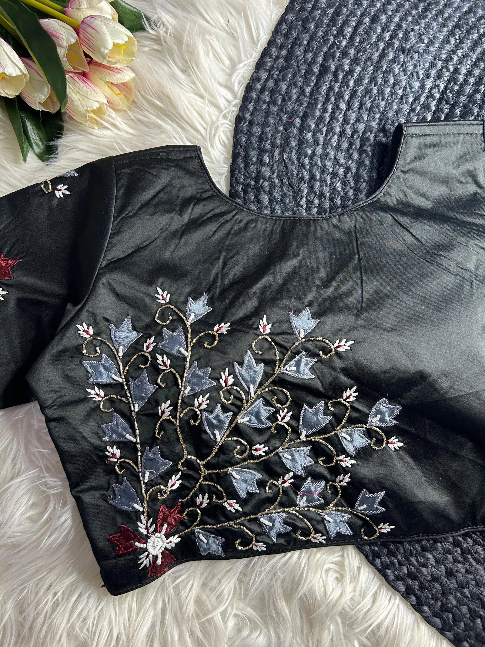 Black jacket with floral embroidery on a textured surface with flowers in the background