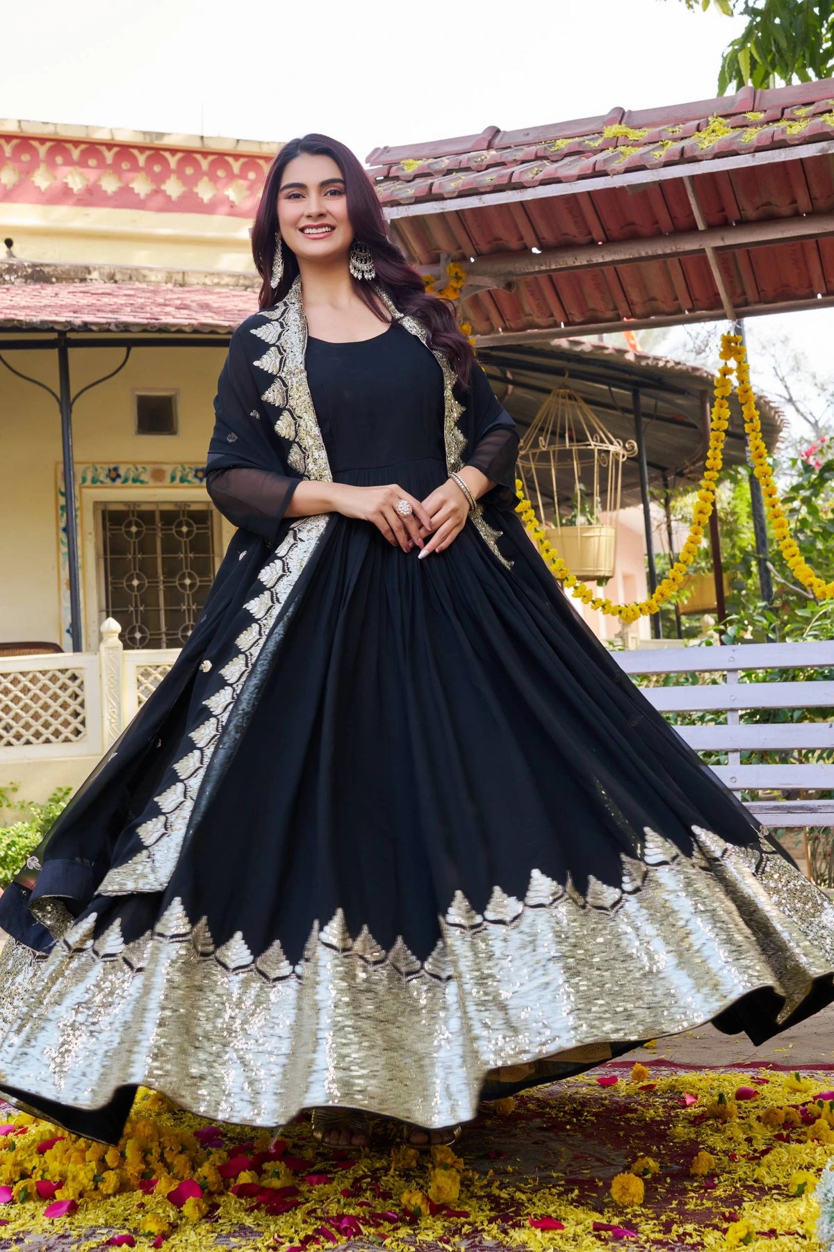 Woman in a black and gold traditional outfit standing outdoors with decorative elements.