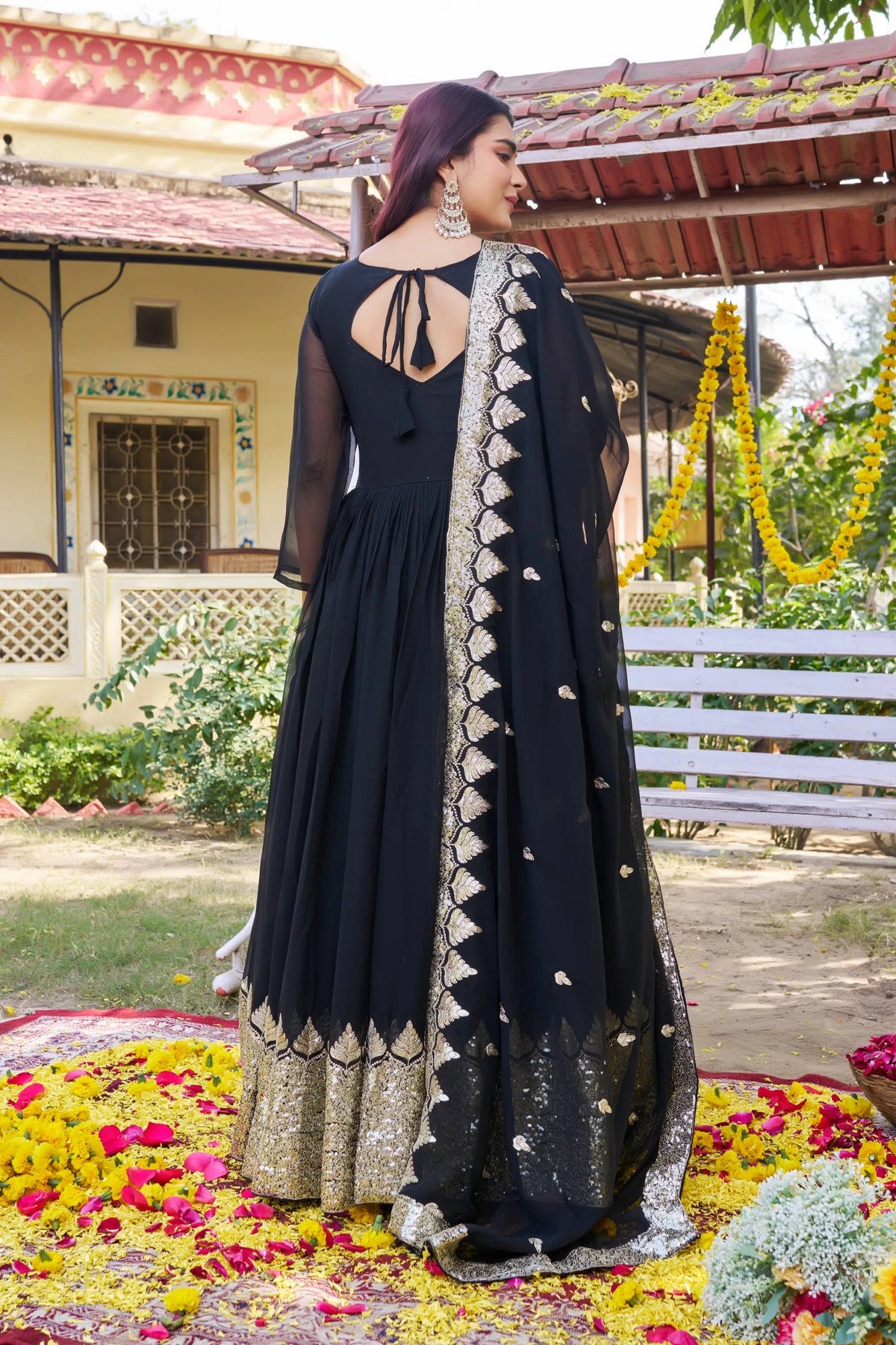Woman in a black and gold traditional outfit standing on a floral carpet with a decorative background.
