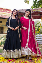Two women in traditional black and pink dresses standing outdoors with a decorative background.