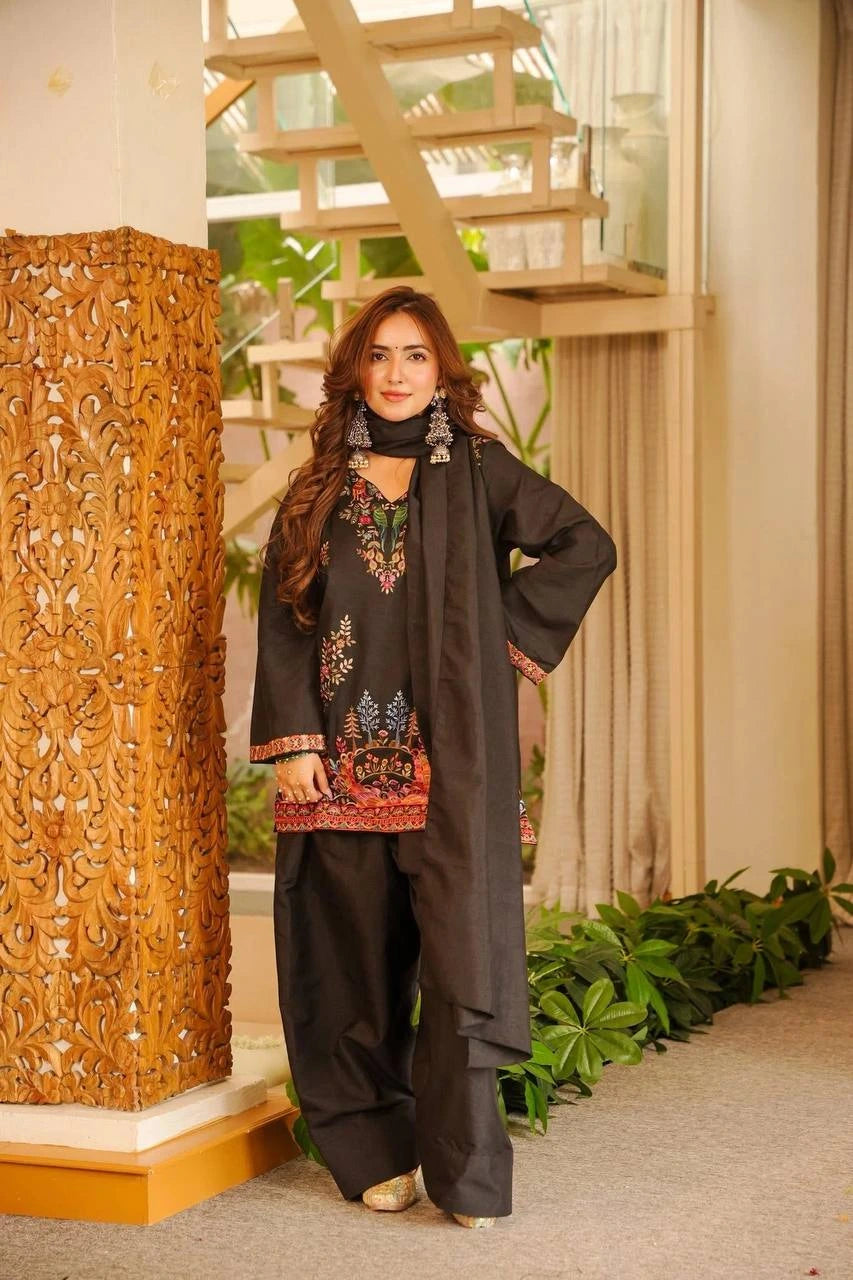 Woman in traditional outfit standing in a decorative indoor setting with plants and wooden columns.