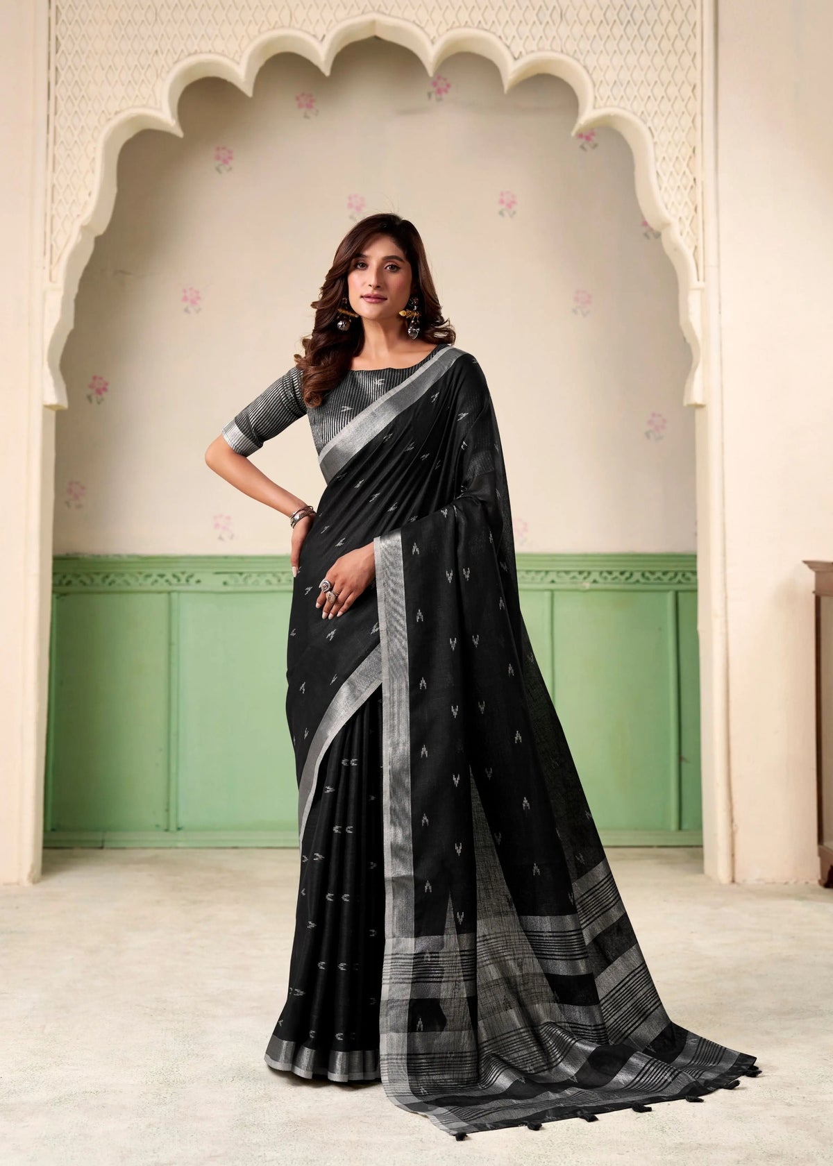 Woman wearing a black saree with a white border in an ornate room.