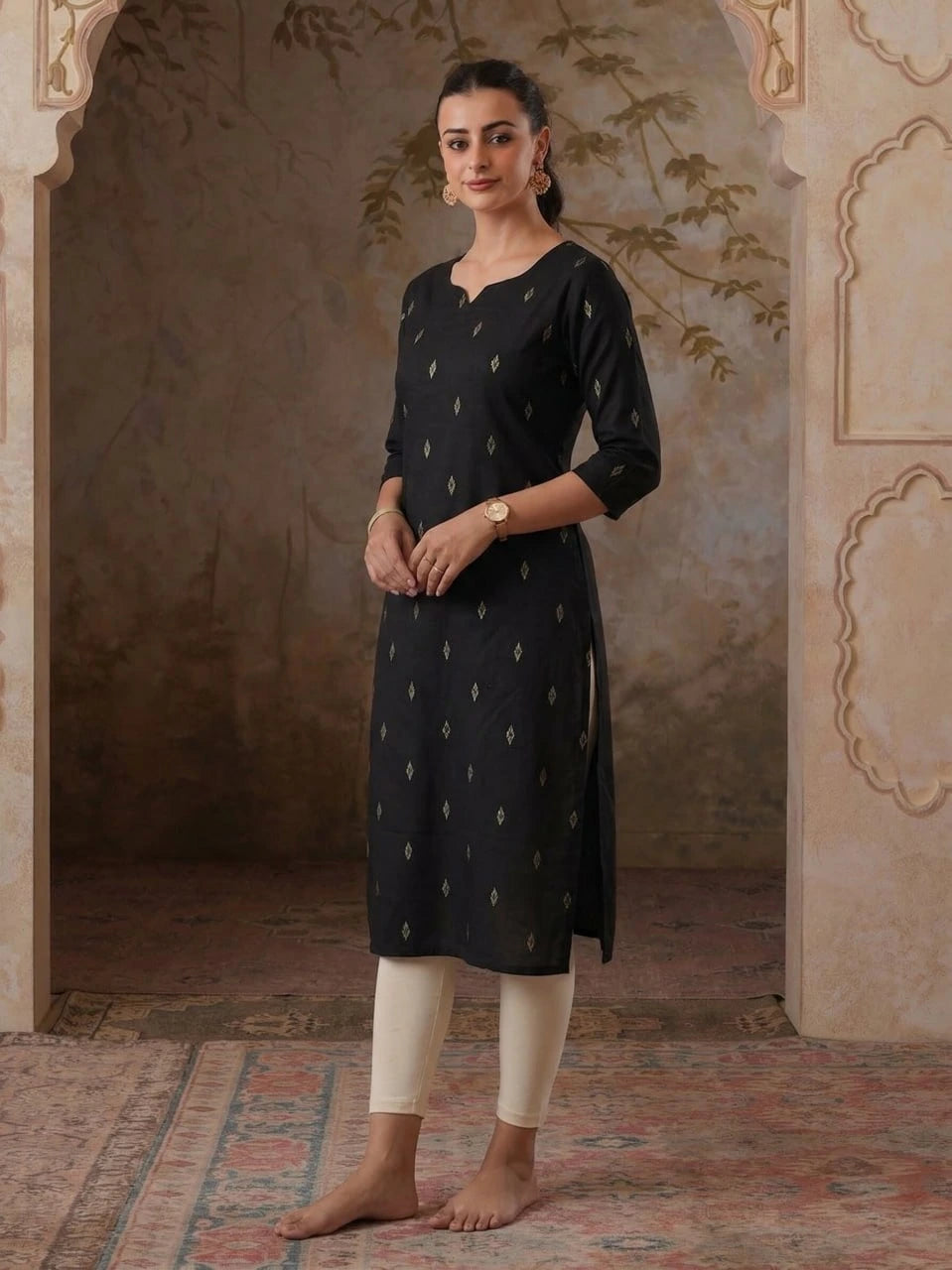 Woman wearing a black kurta with white patterns and white pants in an ornate room.