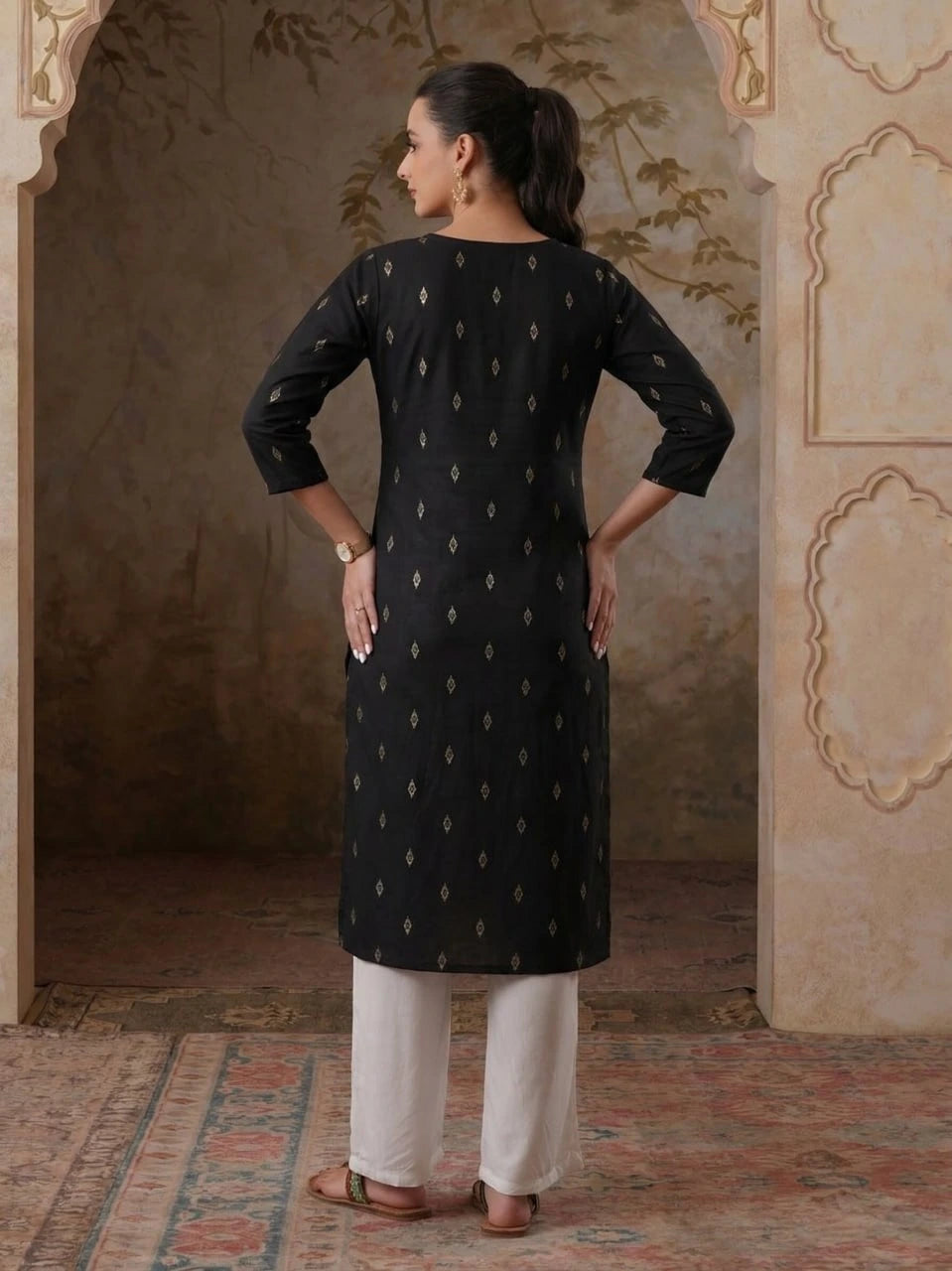 Woman wearing a black kurta with white patterns in an ornate room.