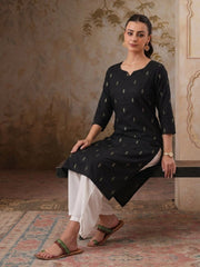 Woman wearing a black kurta with white pants sitting on a decorative rug.