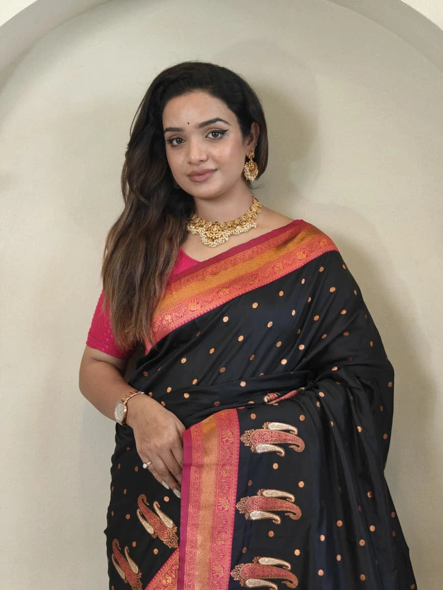 Woman wearing a black saree with pink and gold patterns against a plain background