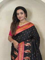 Woman wearing a black saree with pink and gold patterns against a plain background