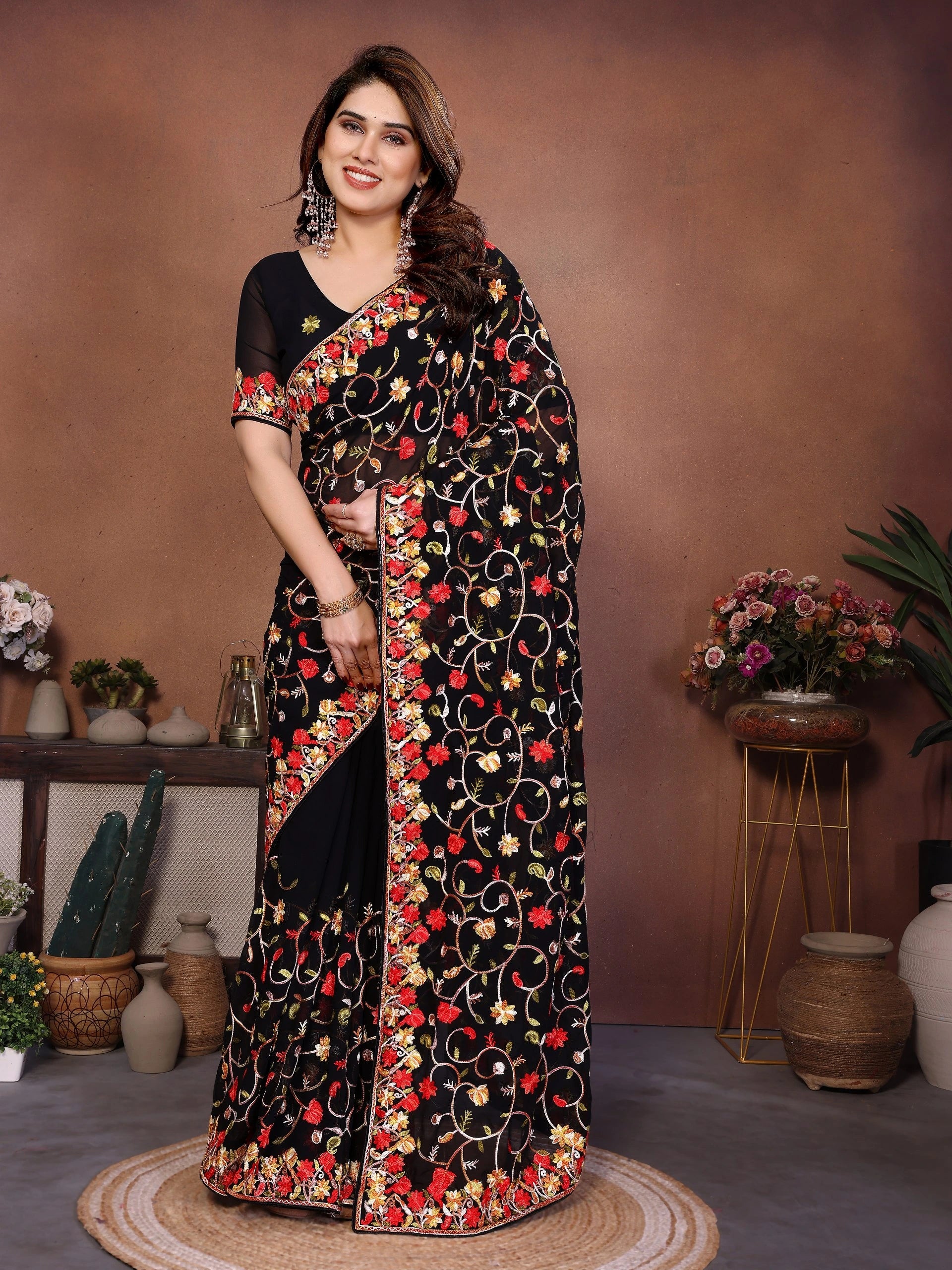 Woman wearing a black saree with red and gold floral patterns in a decorated room.