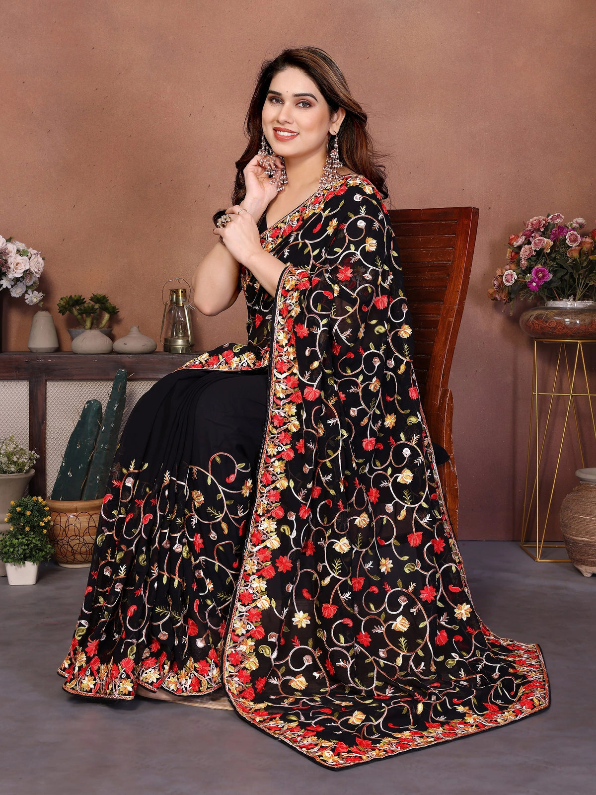 Woman wearing a black saree with floral patterns in a decorated room.