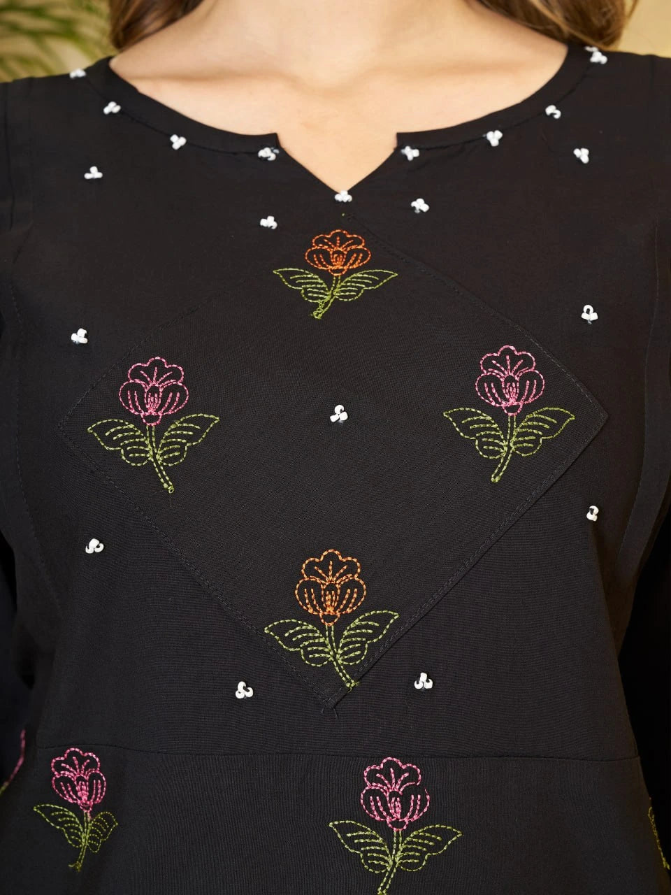 Black top with colorful floral embroidery on a blurred background