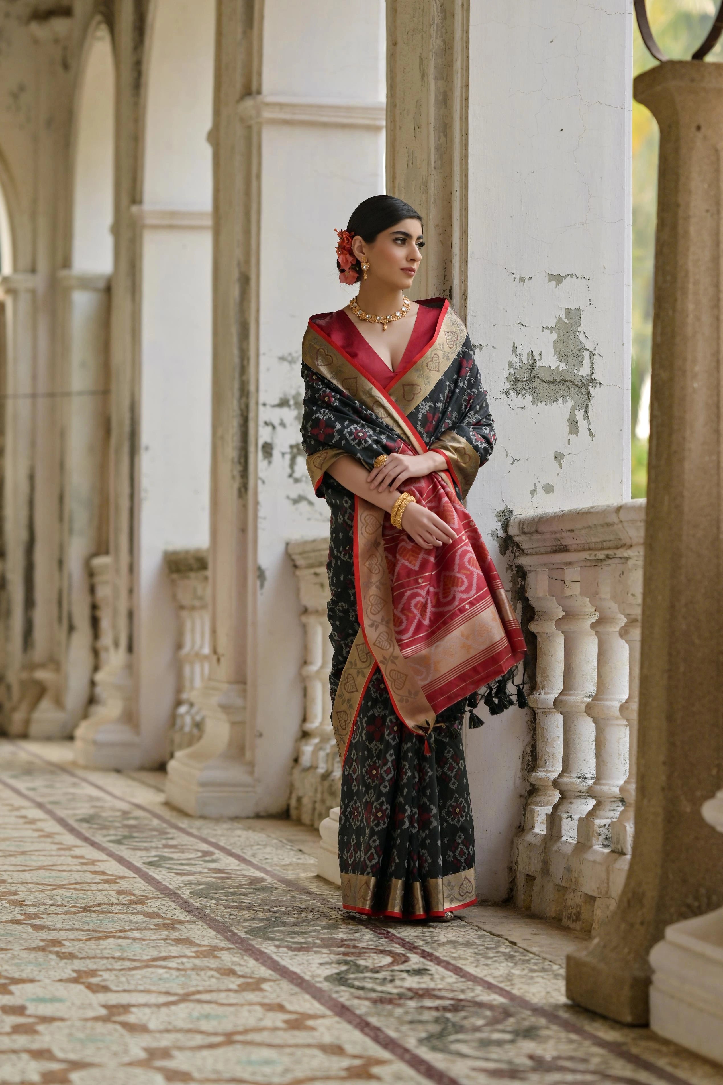 Woman in traditional attire standing in an elegant indoor setting with marble columns.