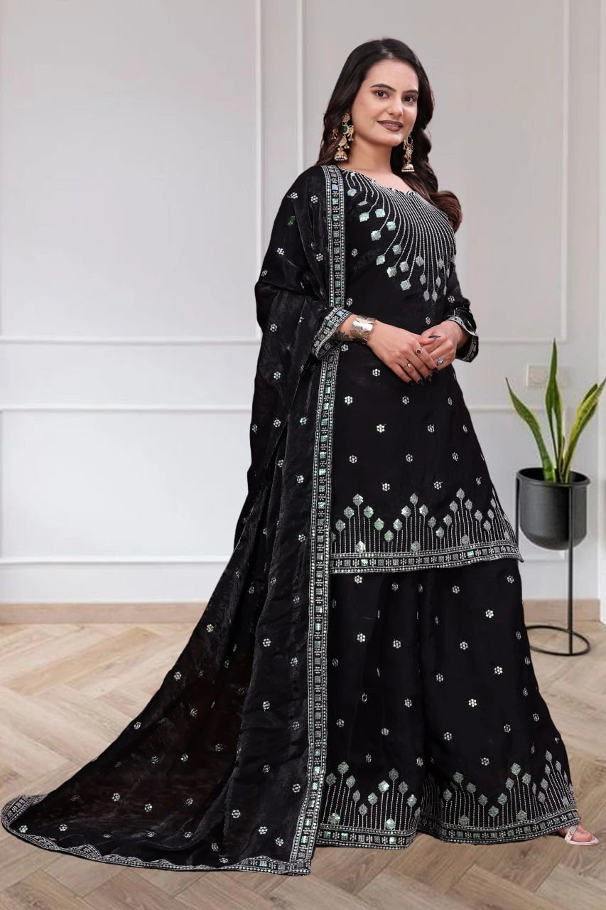 Woman wearing a black traditional outfit with silver embroidery in a minimalistic room.