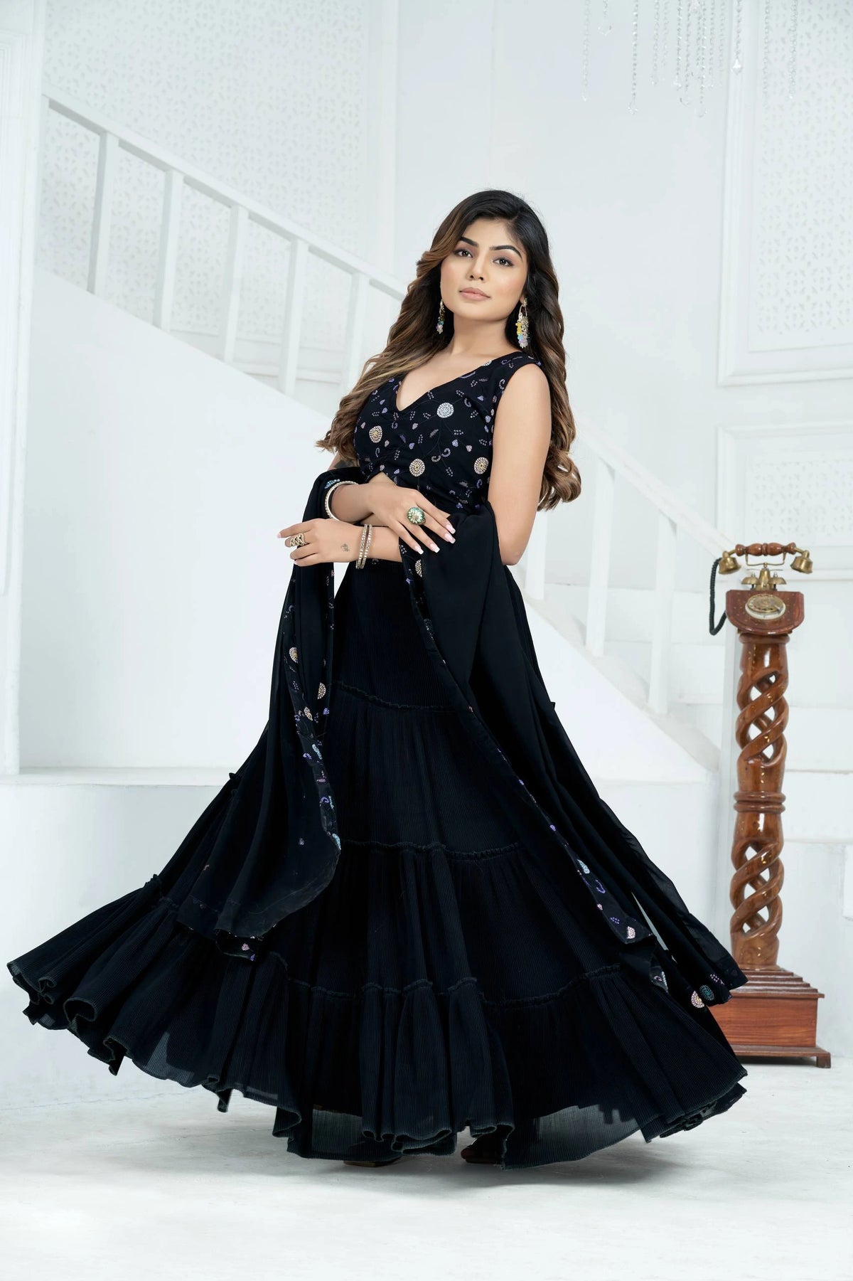 Woman in a black dress with intricate detailing standing against a white background