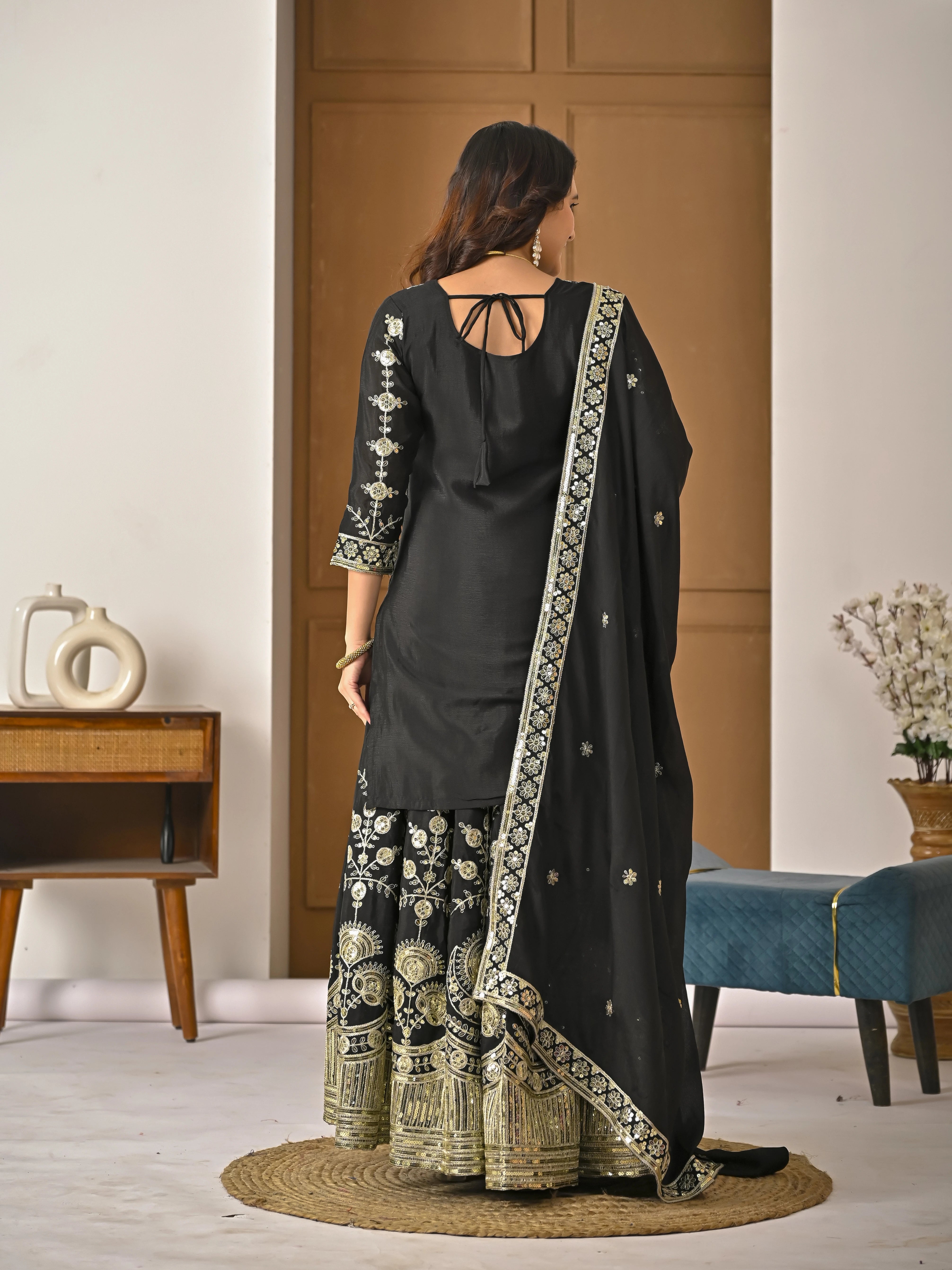 Woman wearing a black traditional outfit with gold embroidery in a room.