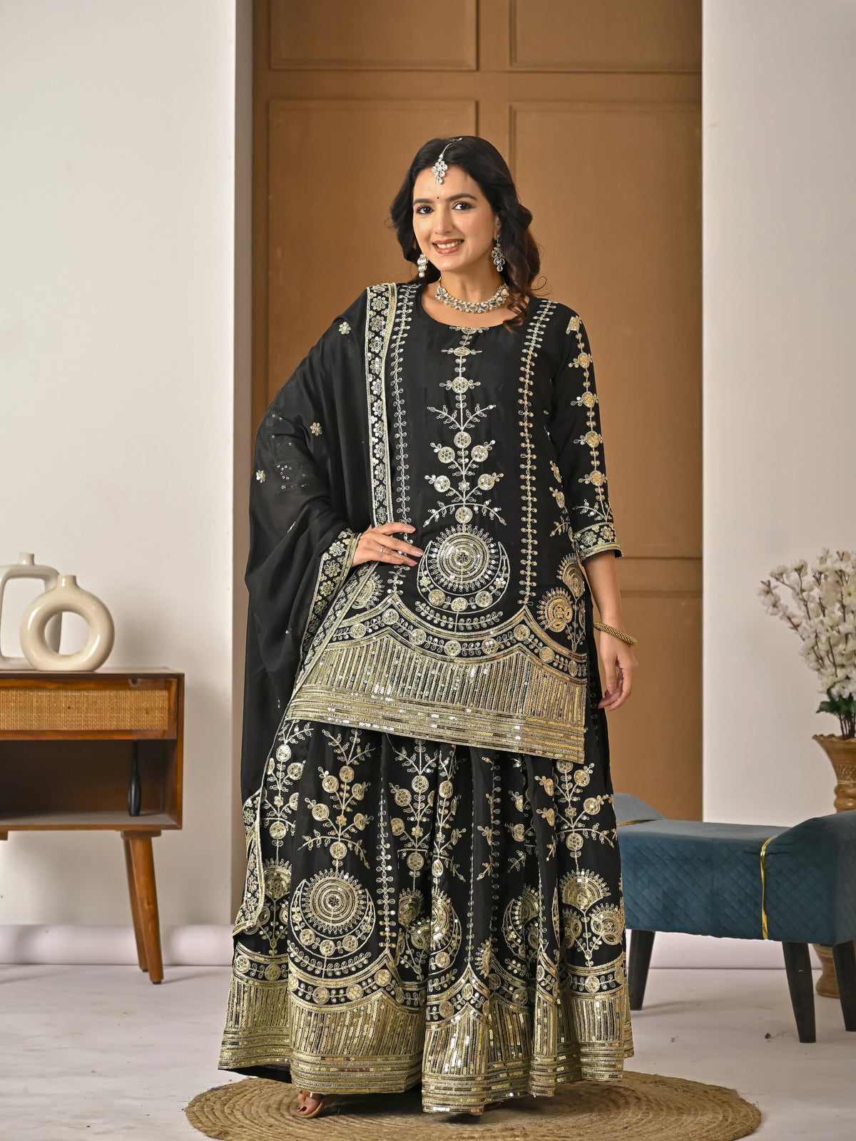 Woman wearing a black and gold embroidered traditional outfit in a room with wooden paneling.