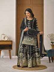 Woman in traditional black and gold embroidered outfit standing in a room with wooden furniture.