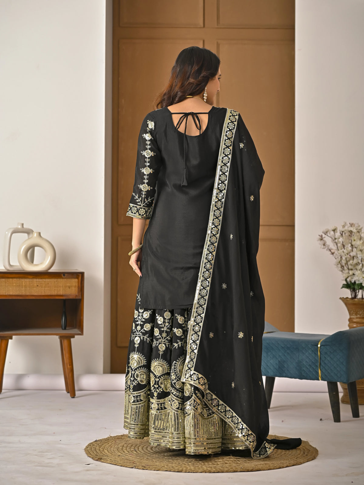 Woman wearing a black traditional outfit with gold embroidery in a room.