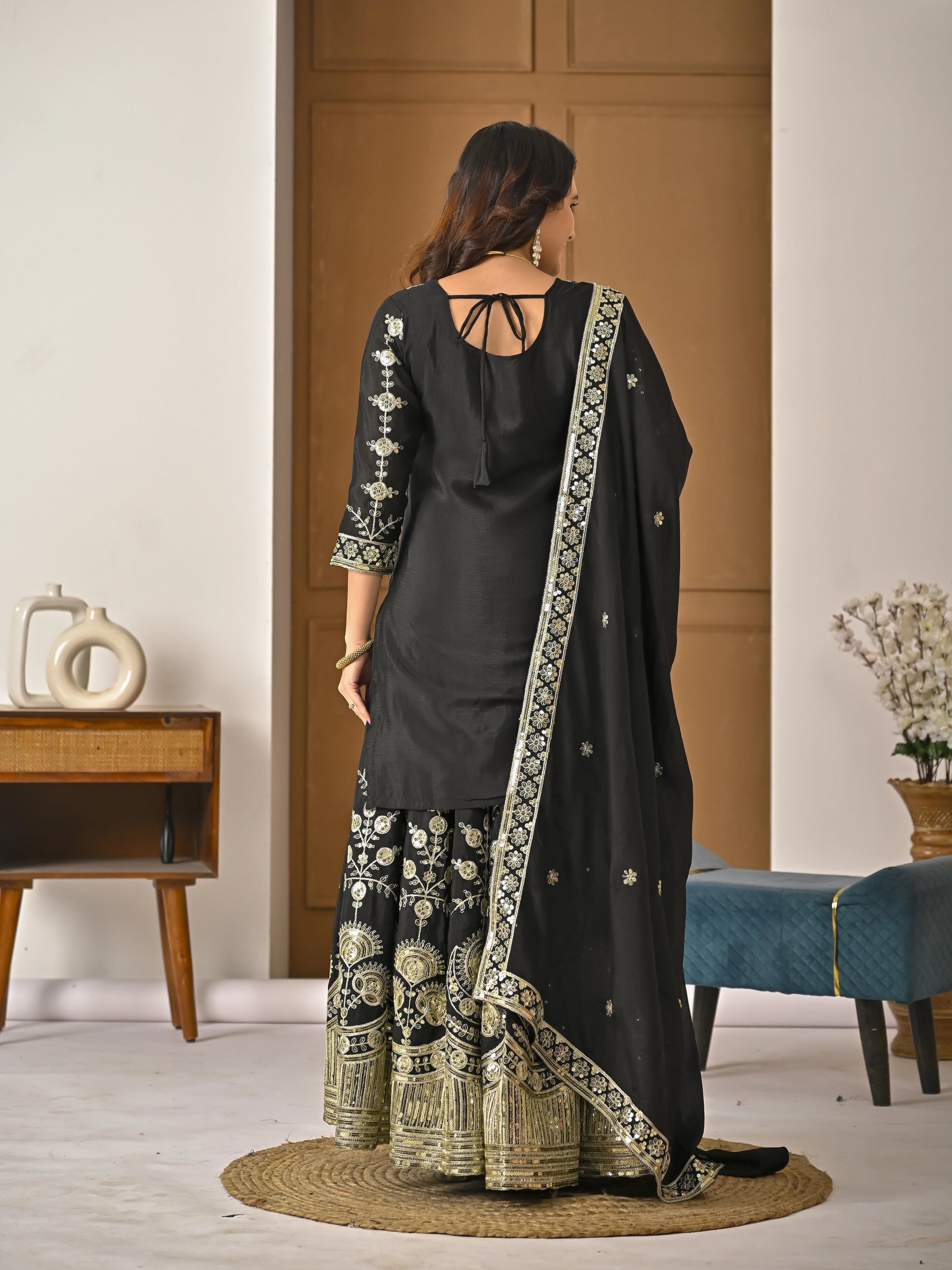 Woman wearing a black traditional outfit with gold embroidery in a room.