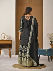 Woman wearing a black traditional outfit with gold embroidery in a room.