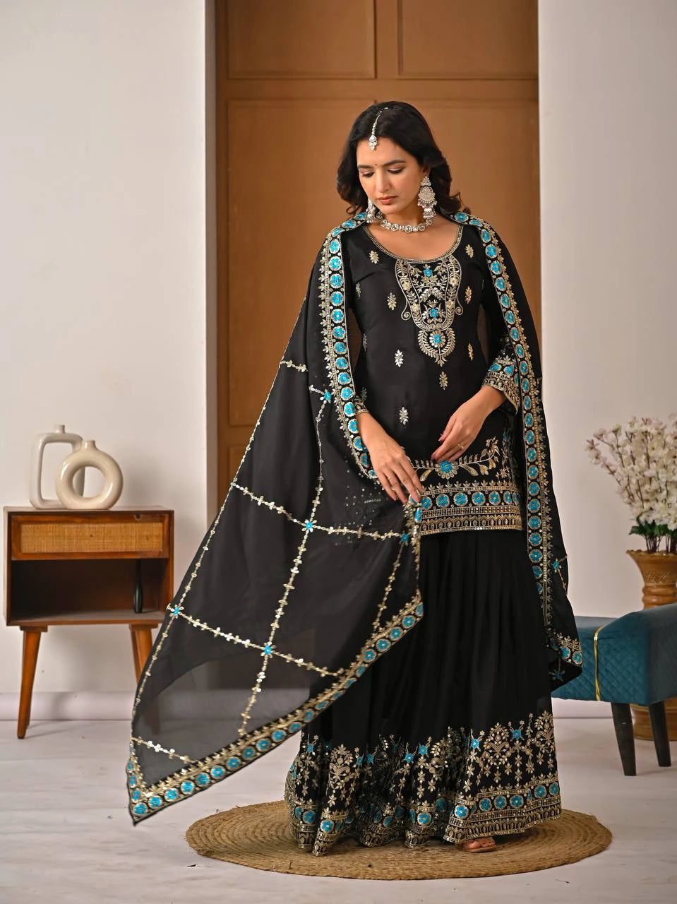 Woman in traditional black and turquoise embroidered outfit standing indoors.