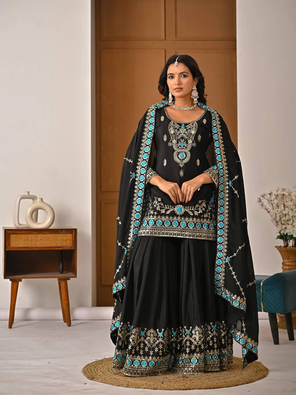 Woman in a black traditional outfit with turquoise embellishments in a room setting.