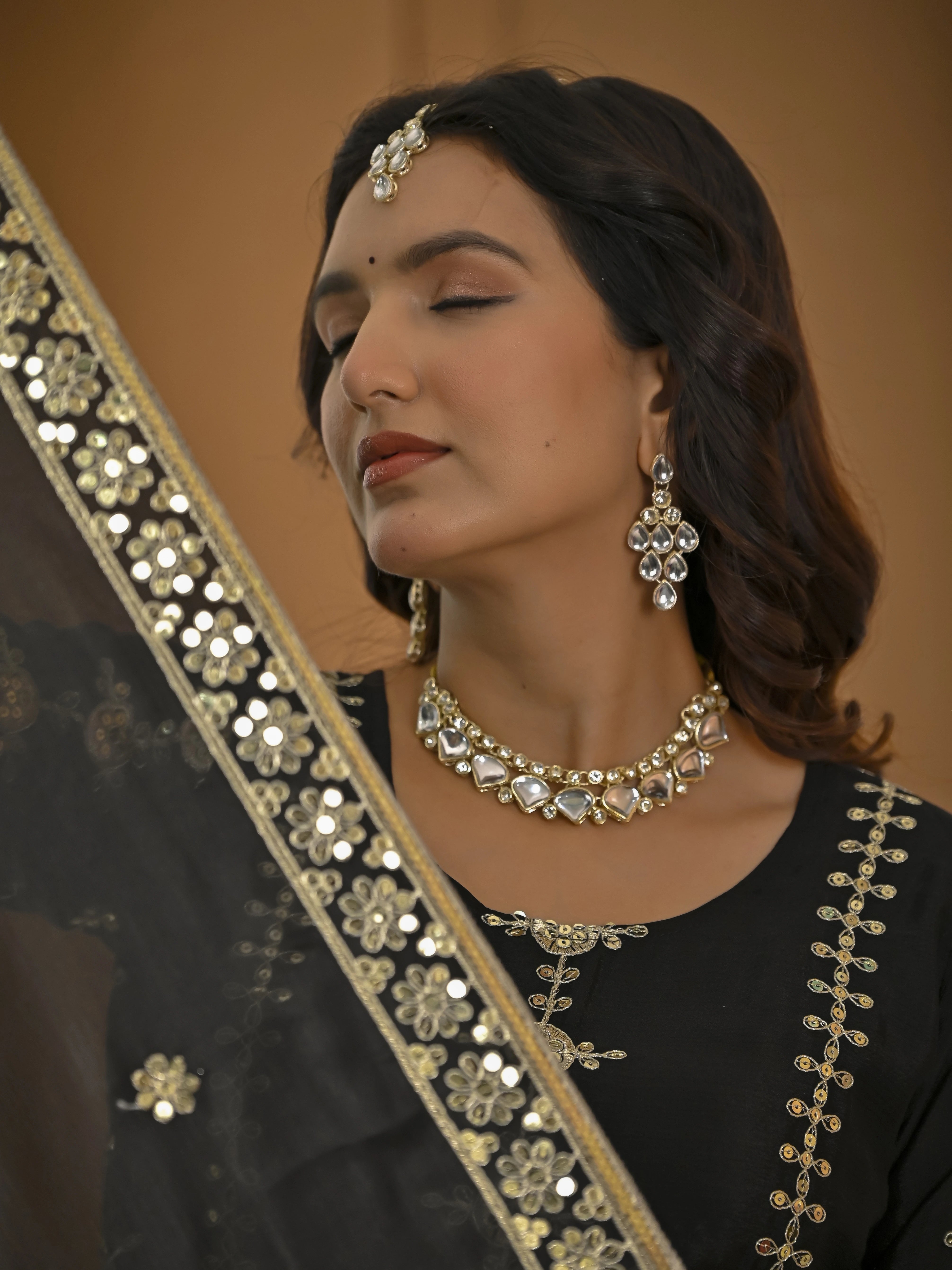 Woman wearing traditional jewelry with a black outfit and gold embroidery.
