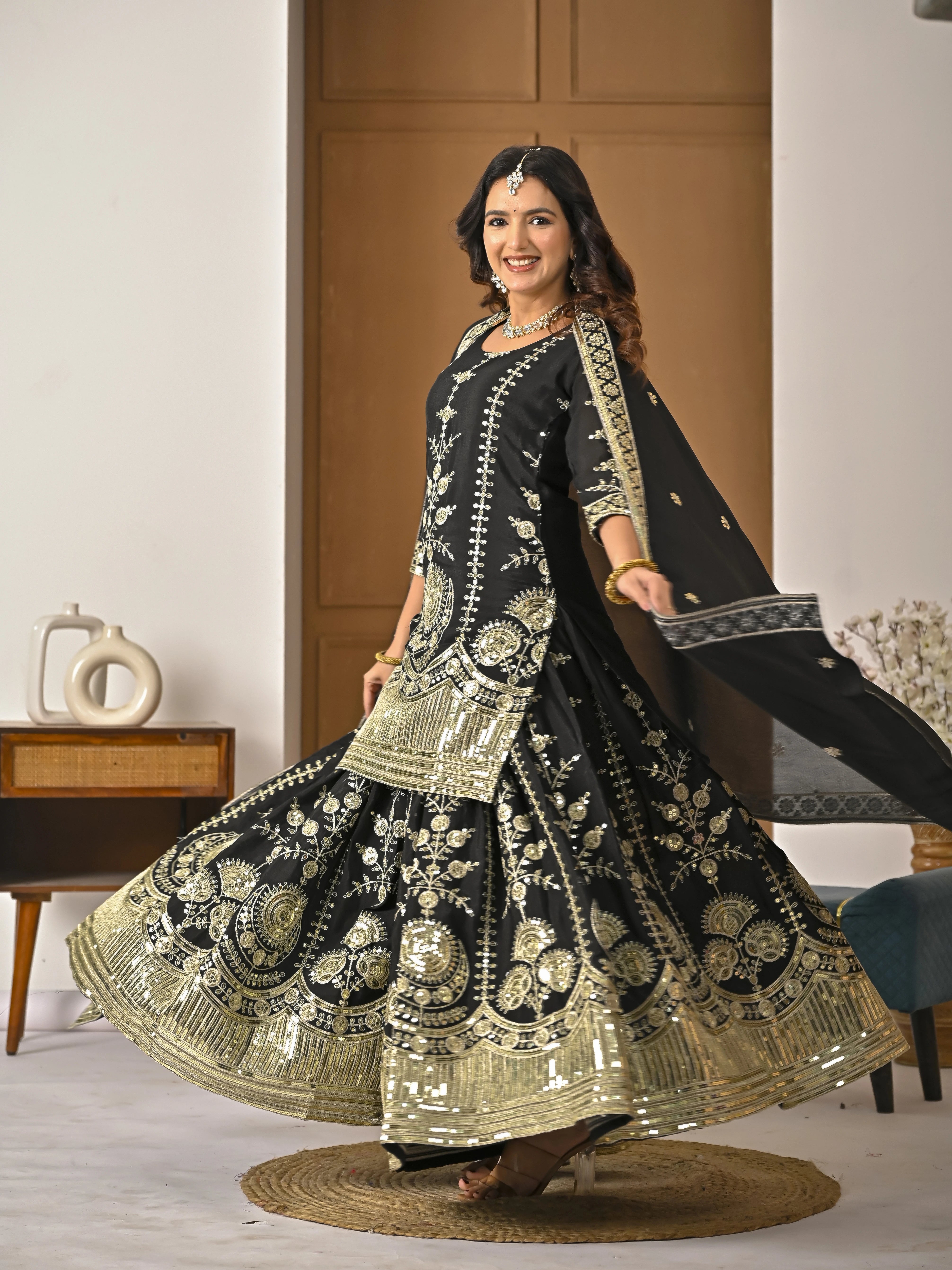 Woman in a black and gold embroidered traditional outfit in a room setting.