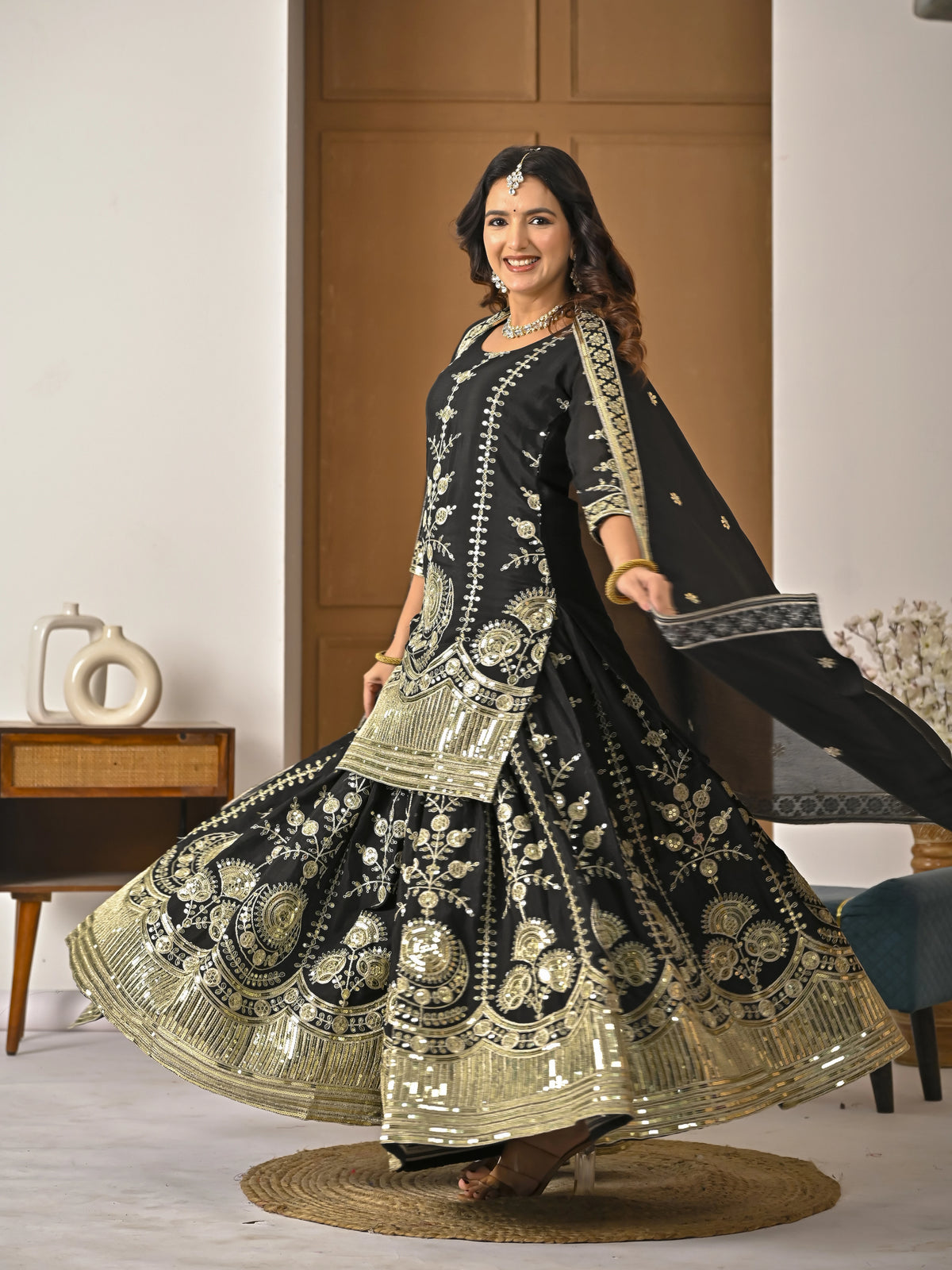 Woman in a black and gold embroidered traditional outfit in a room setting.