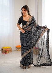 Woman wearing a black saree with a floral blouse, standing indoors.