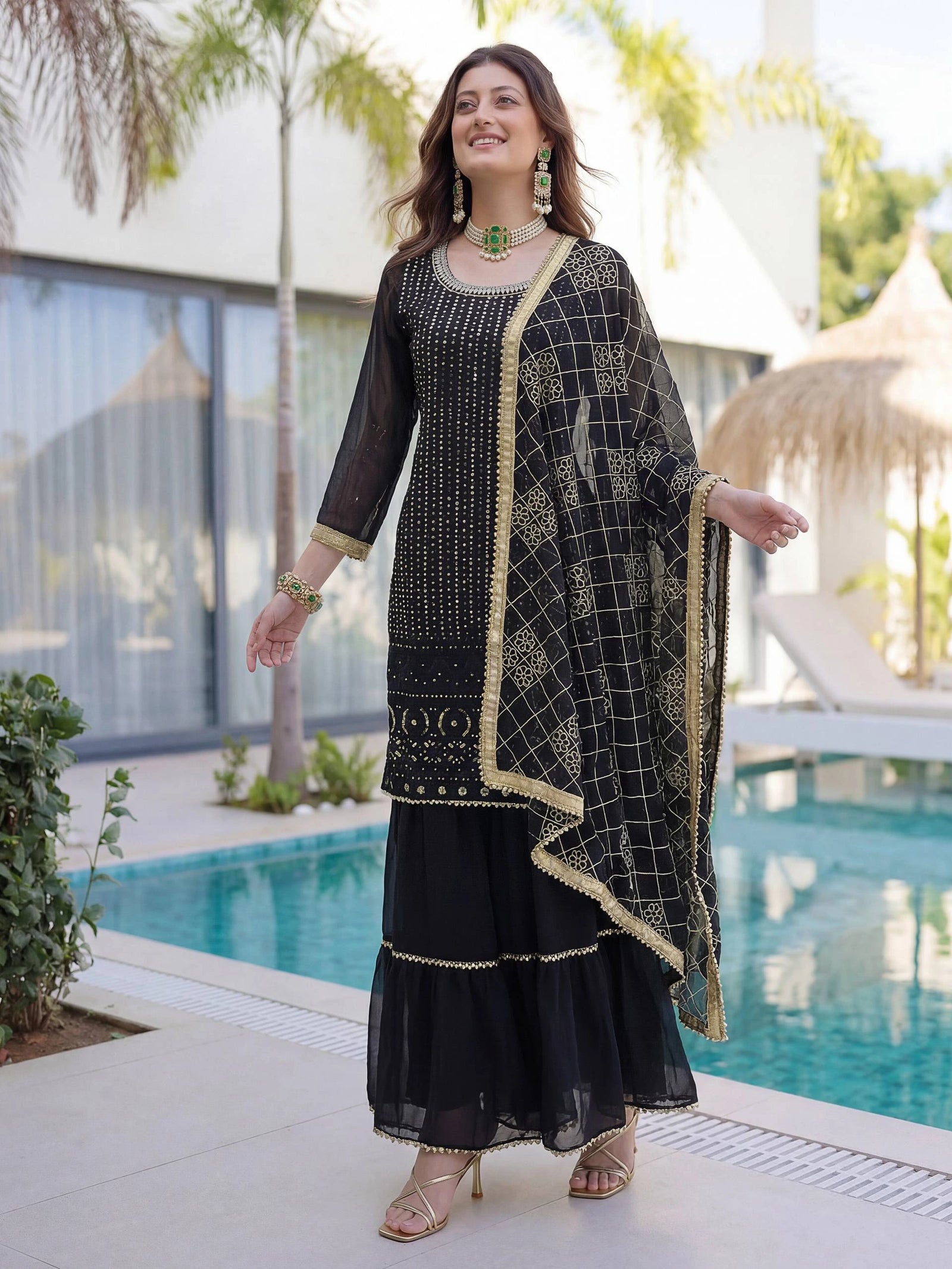Woman in a black and gold traditional outfit standing by a pool.