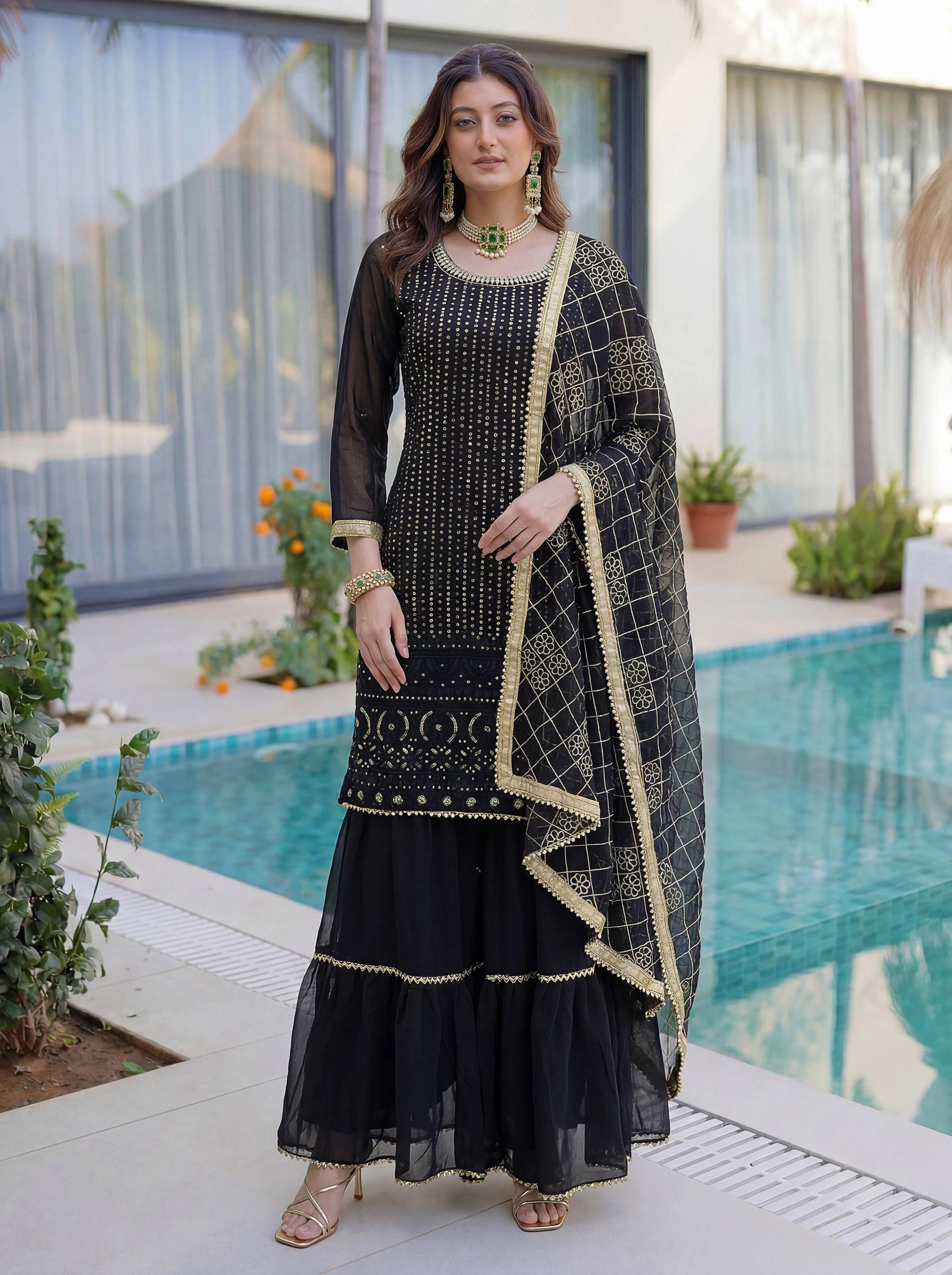 Woman in a black and gold traditional outfit standing by a pool.