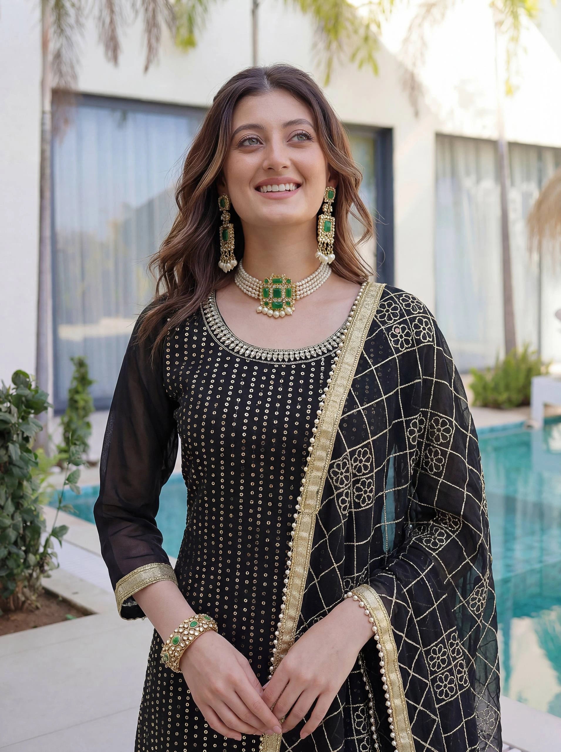 Woman in traditional black and gold outfit with jewelry by a pool