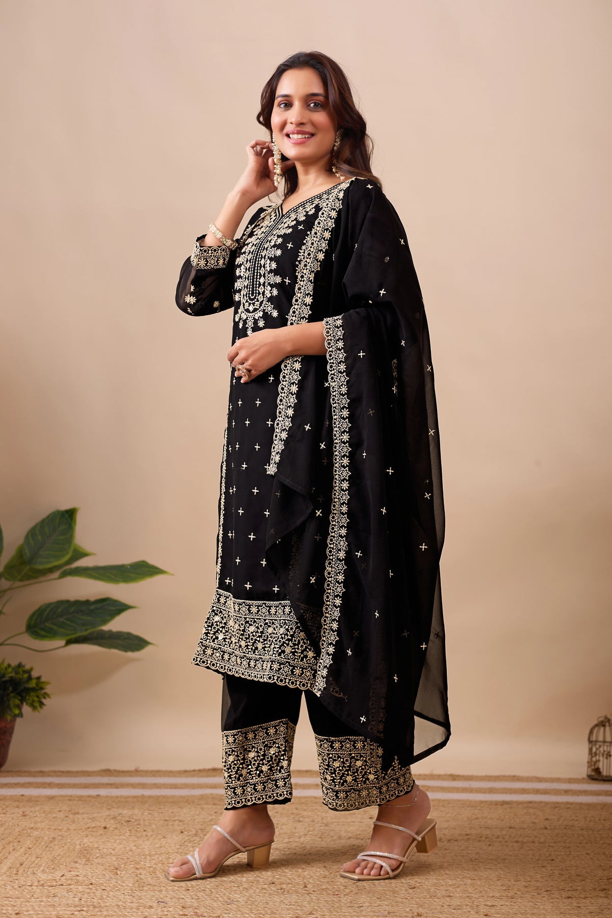 Woman wearing a black traditional outfit with silver embroidery against a beige background
