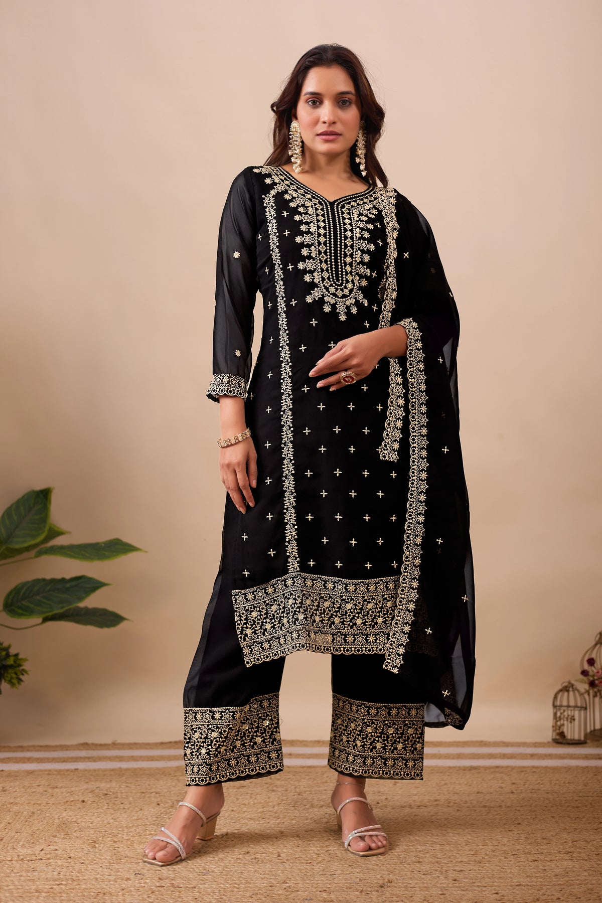 Woman wearing a black embroidered traditional outfit with gold details on a beige background
