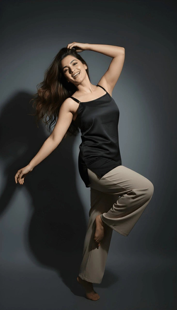 Woman posing in a black tank top and beige pants against a dark background