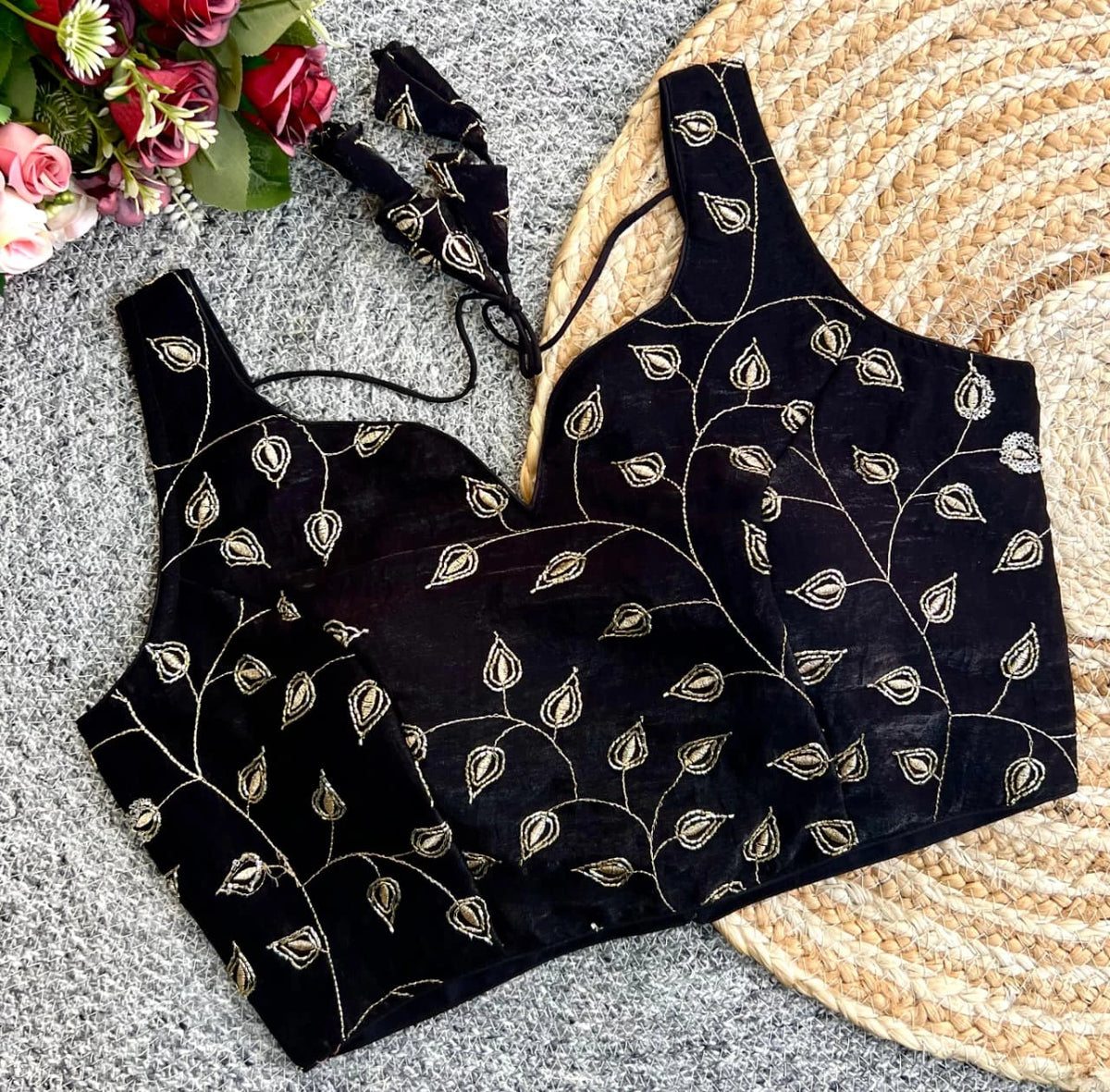 Black embroidered top on a textured surface with flowers and a hat in the background