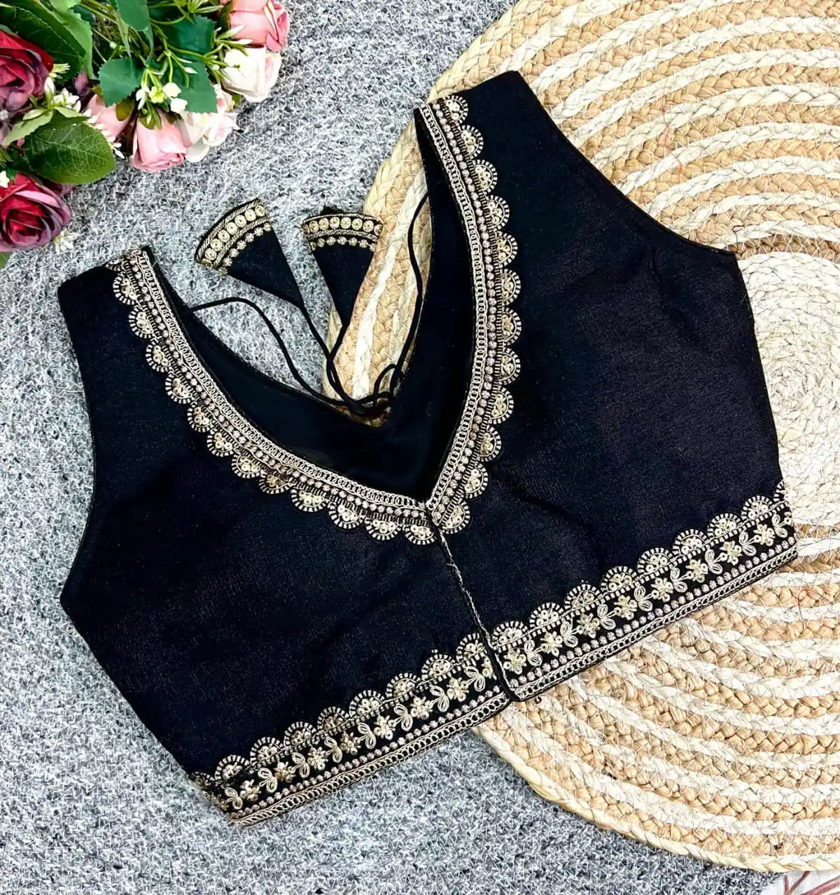 Black blouse with intricate gold embroidery on a textured surface with flowers and a fan.