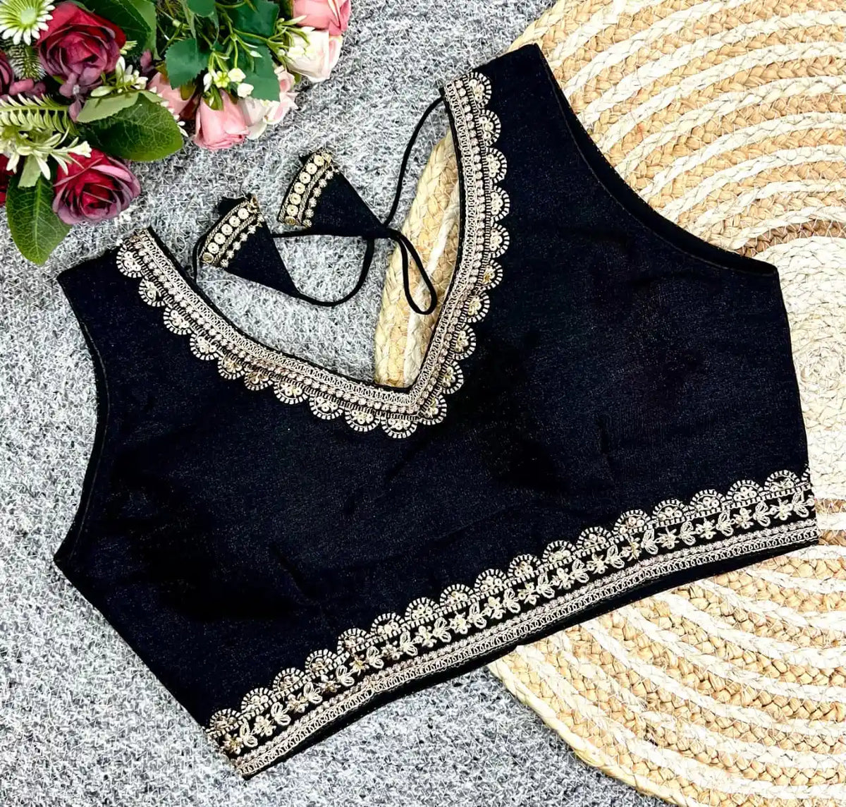Black blouse with silver embroidery on a textured surface with flowers in the corner