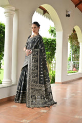 Woman in a black and white patterned saree standing in a decorative archway.