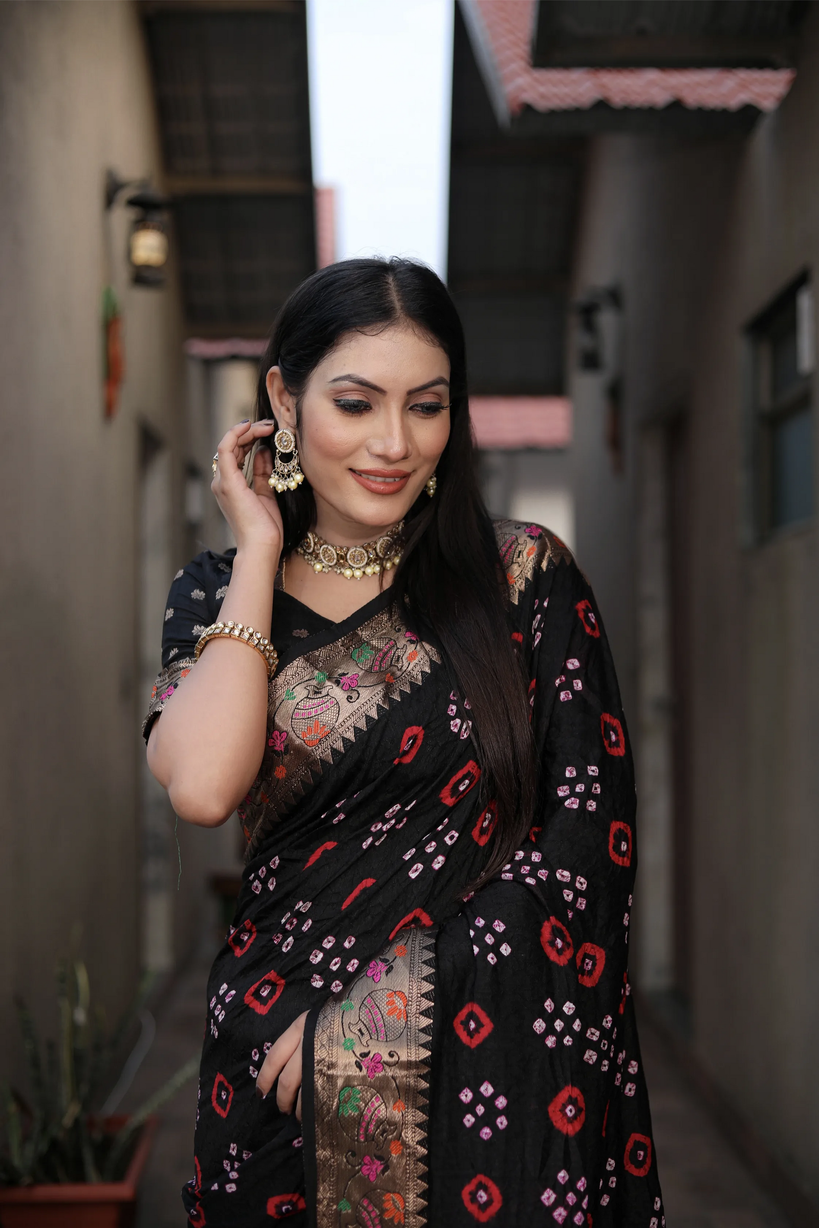 Woman wearing a black saree with red and pink patterns in an outdoor setting
