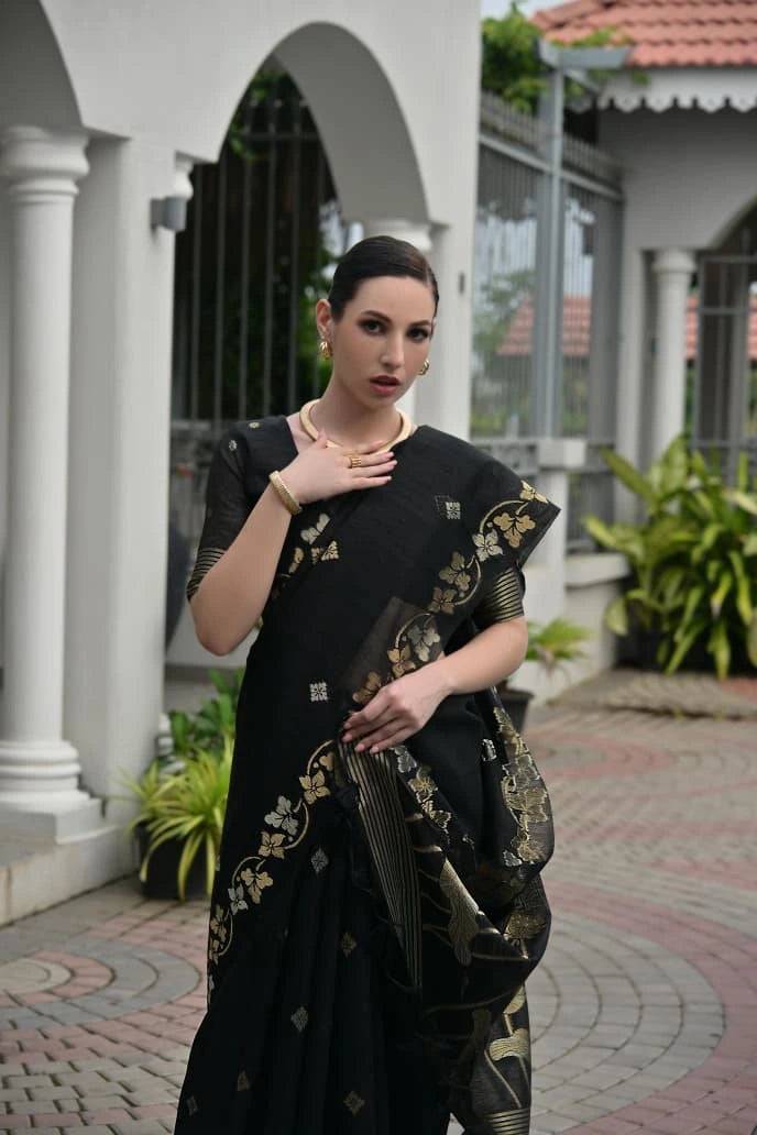 Woman wearing a black saree with gold patterns standing outdoors.