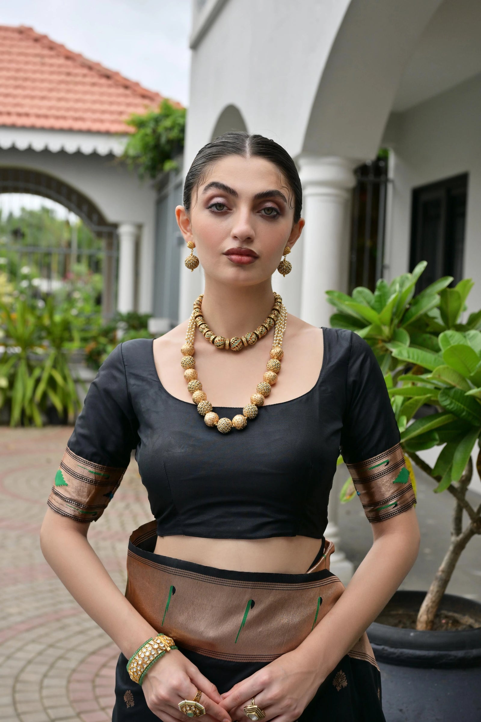 Woman in traditional attire with jewelry standing outdoors.