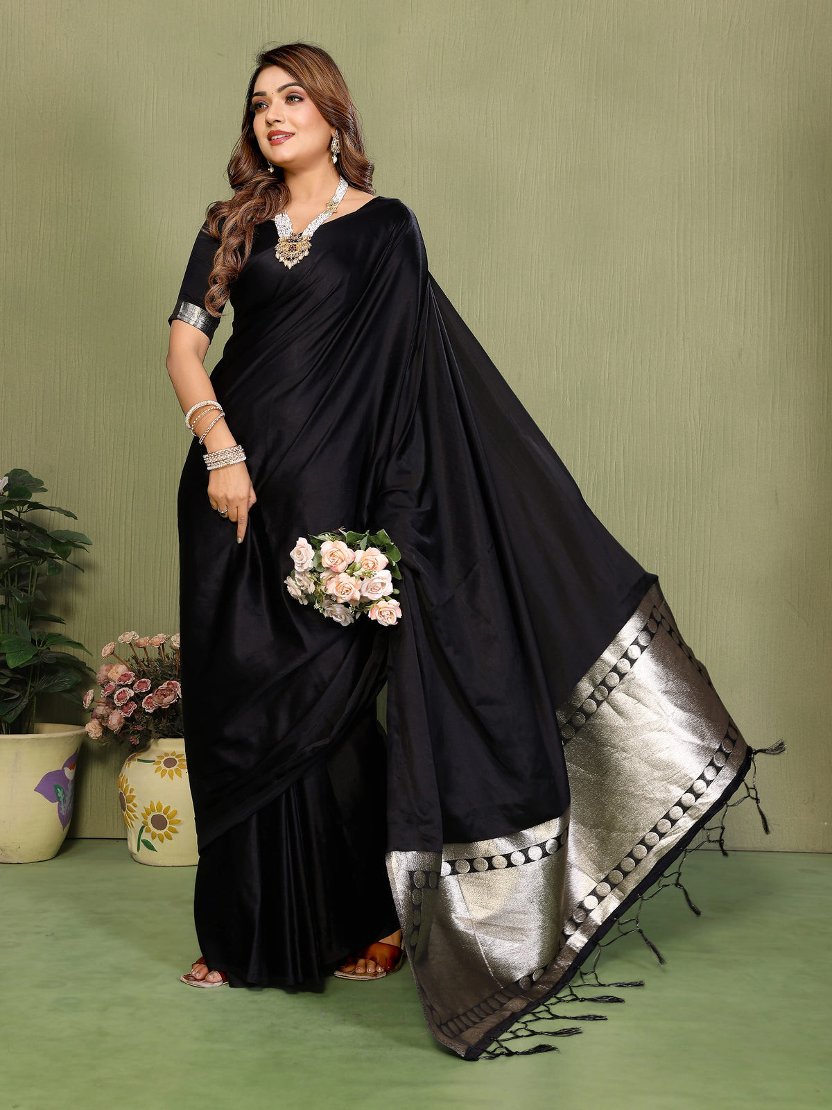 Woman wearing a black saree with silver border on a green background
