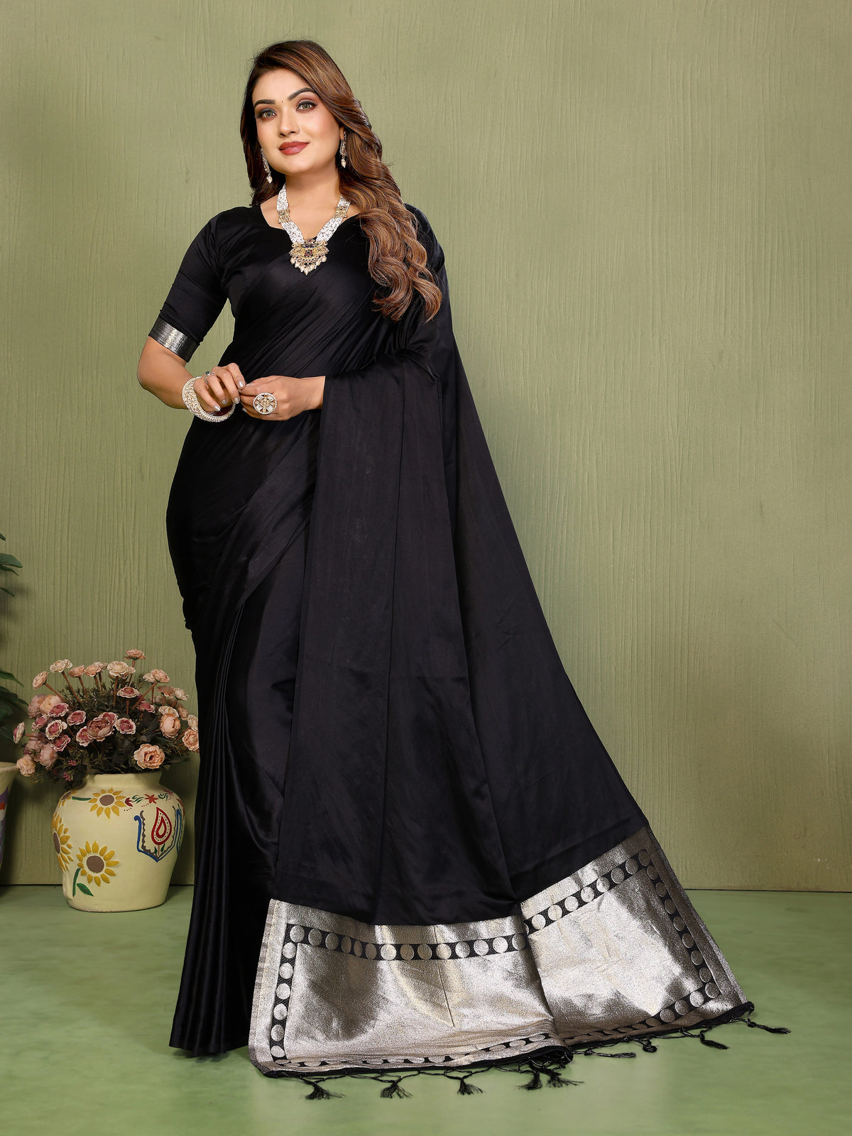 Woman wearing a black saree with silver border against a green background