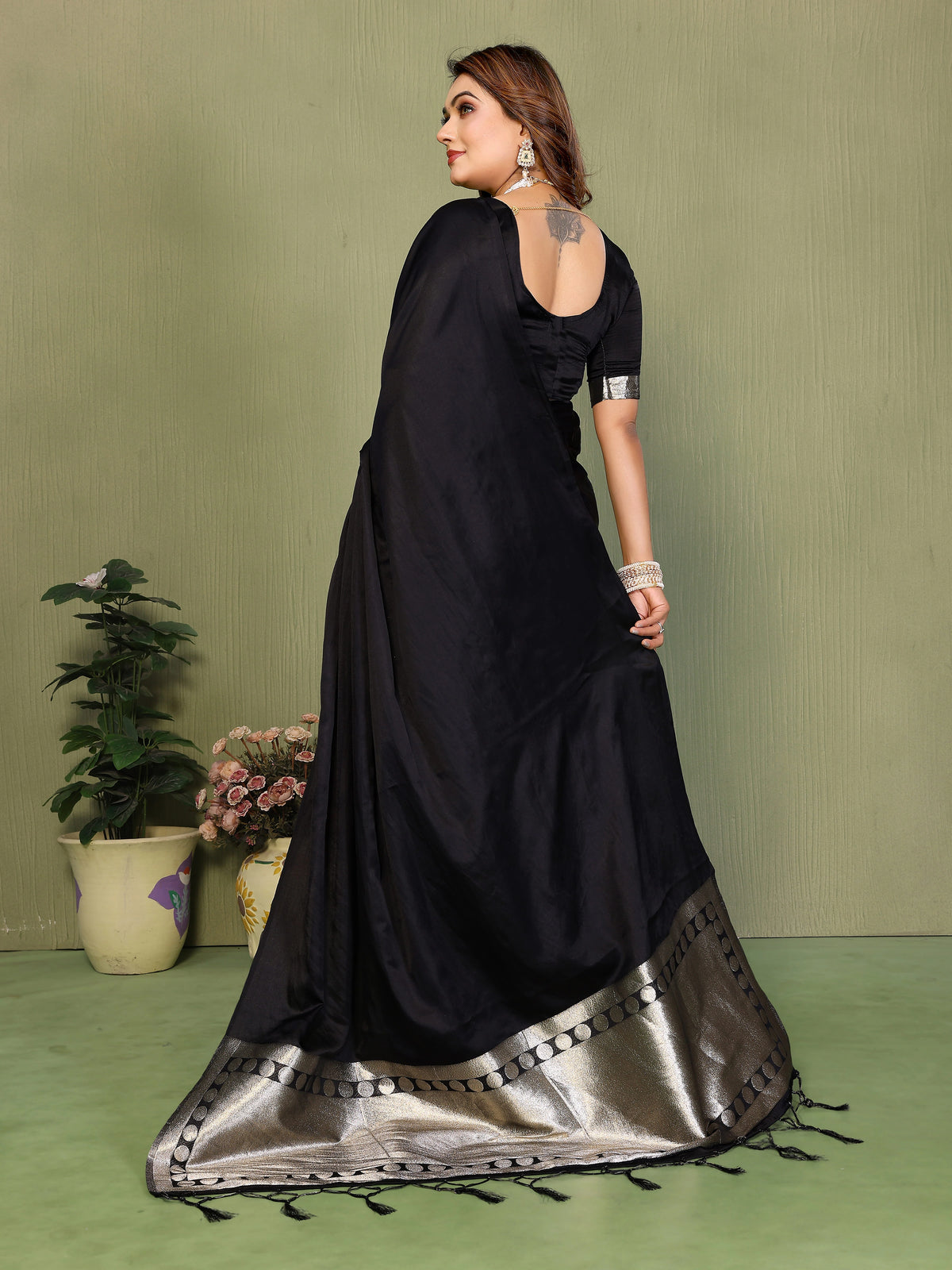 Woman wearing a black saree with silver border on a green background