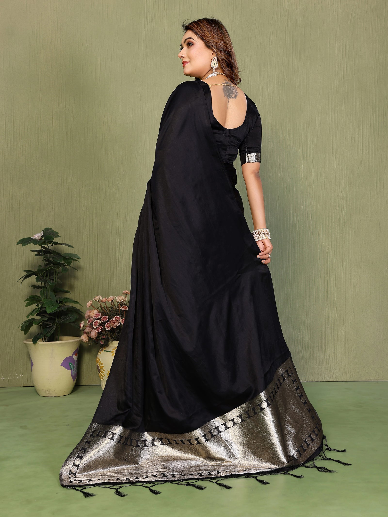 Woman wearing a black saree with silver border on a green background
