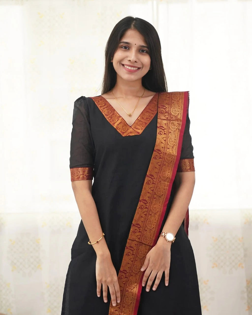 Woman wearing a black saree with a red border against a white background