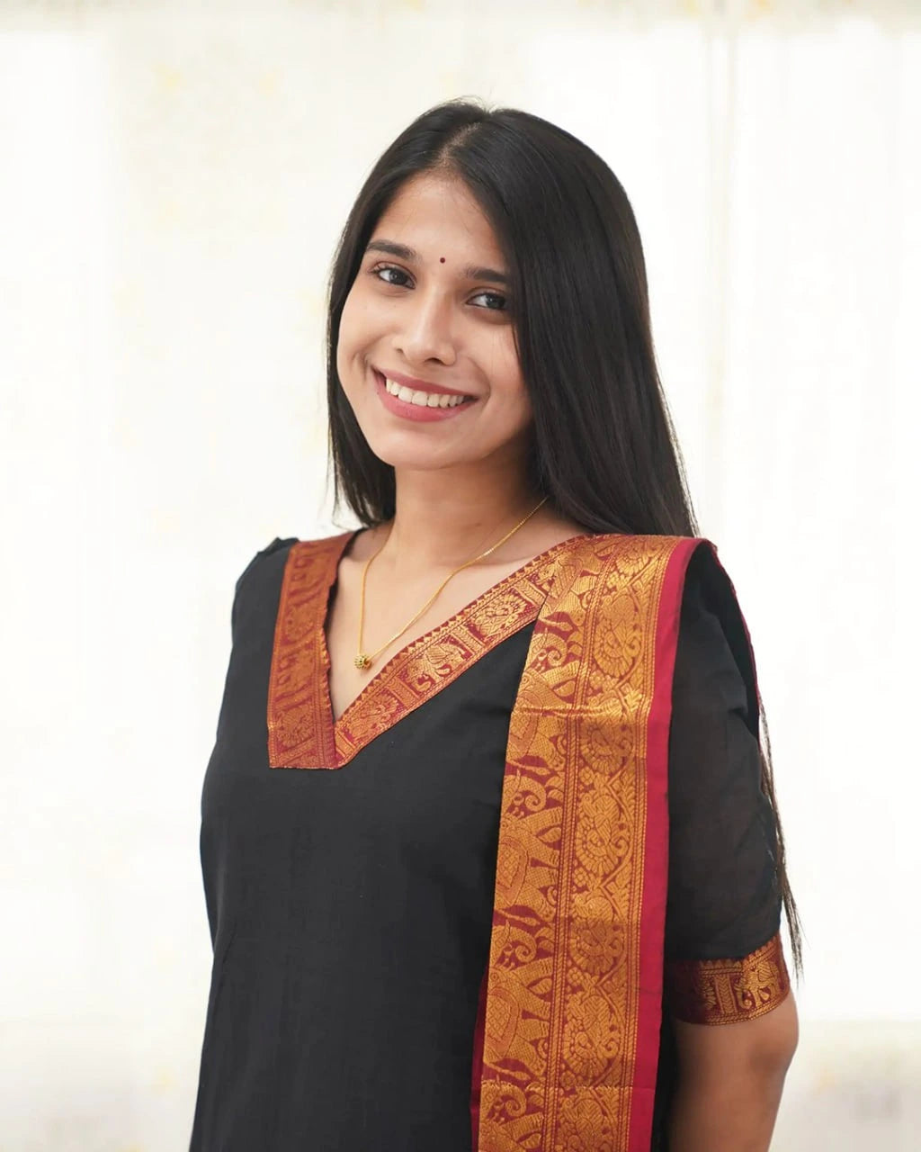 Woman wearing a black traditional outfit with a gold and red border on a white background